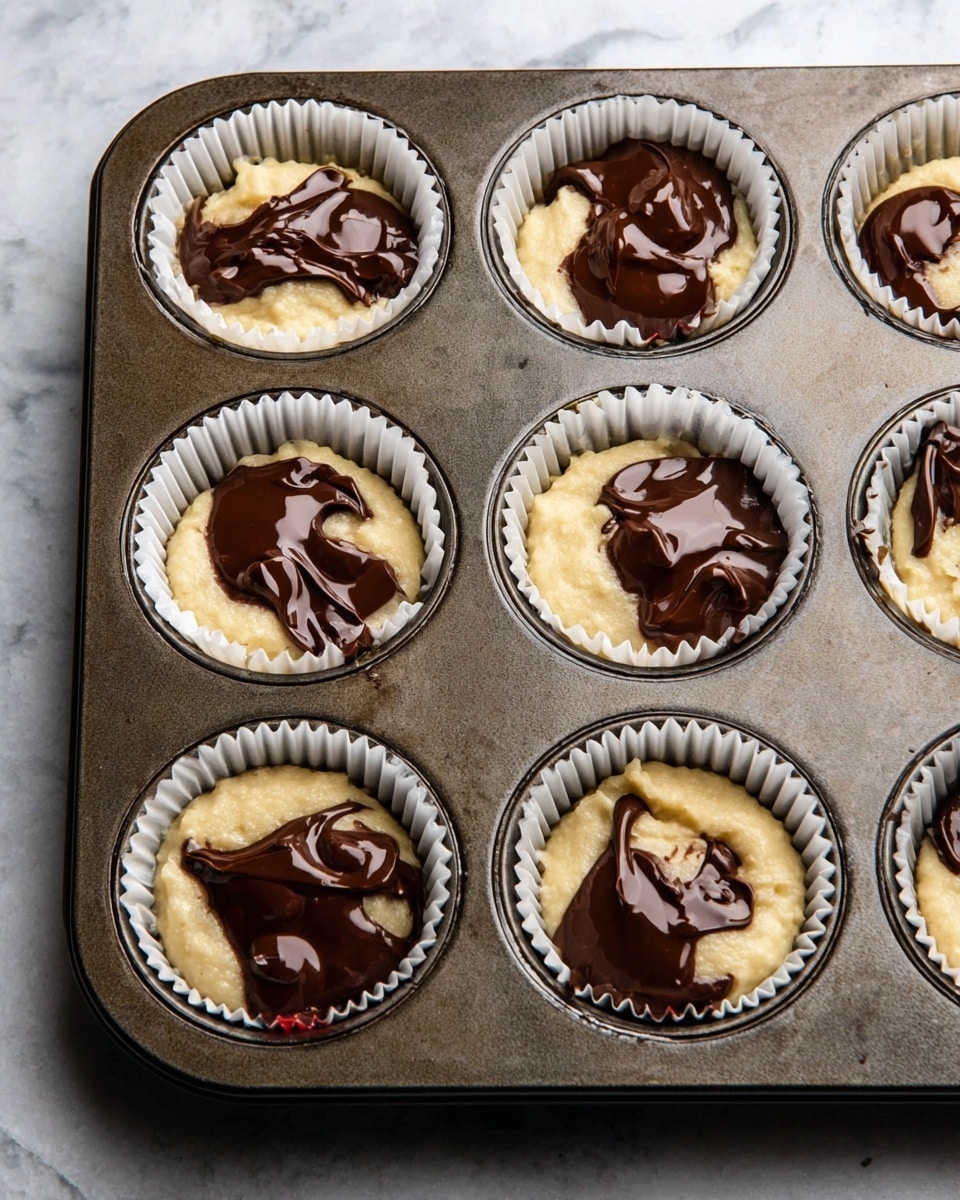 A dark metal muffin tray holds six white paper cupcake liners, each filled with pale yellow batter. On top of the batter in every cup, there is a thick, shiny layer of melted chocolate, unevenly spread and glossy. The tray rests on a white marbled surface, with the chocolate's smooth, rich brown color contrasting with the soft, creamy batter beneath. photo taken with an iphone --ar 4:5 --v 7