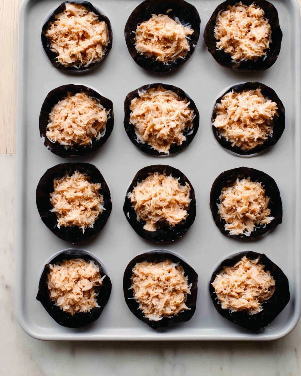 A baking tray with 12 round cups, each lined with black seaweed sheets forming small cups inside the white tray. Each seaweed cup is filled with a light brown shredded filling, roughly piled in the center. The tray is placed on a white marbled surface. The seaweed contrasts sharply with the pale filling and the bright white tray, creating a clean, simple look. photo taken with an iphone --ar 4:5 --v 7