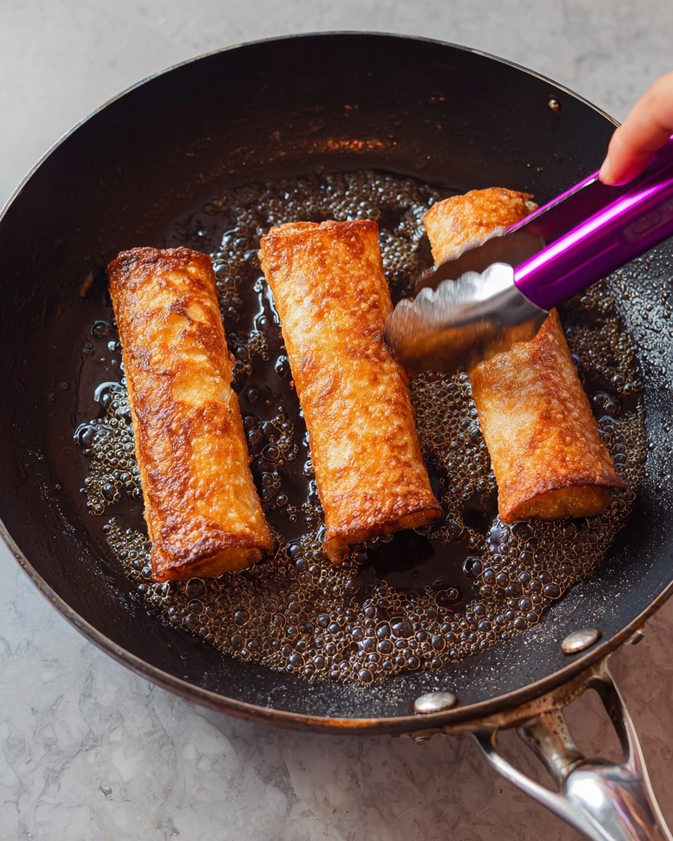 The image shows three golden brown rolled pieces of food frying in a black pan with shiny oil bubbles around them. Each roll has a crispy, slightly textured surface with a warm brown color. A pair of purple tongs held by a woman's hand is gently lifting one roll, highlighting the slightly rough and crispy outer layer. The pan handle is silver and shiny, and the surface under the pan has a white marbled texture background. photo taken with an iphone --ar 4:5 --v 7