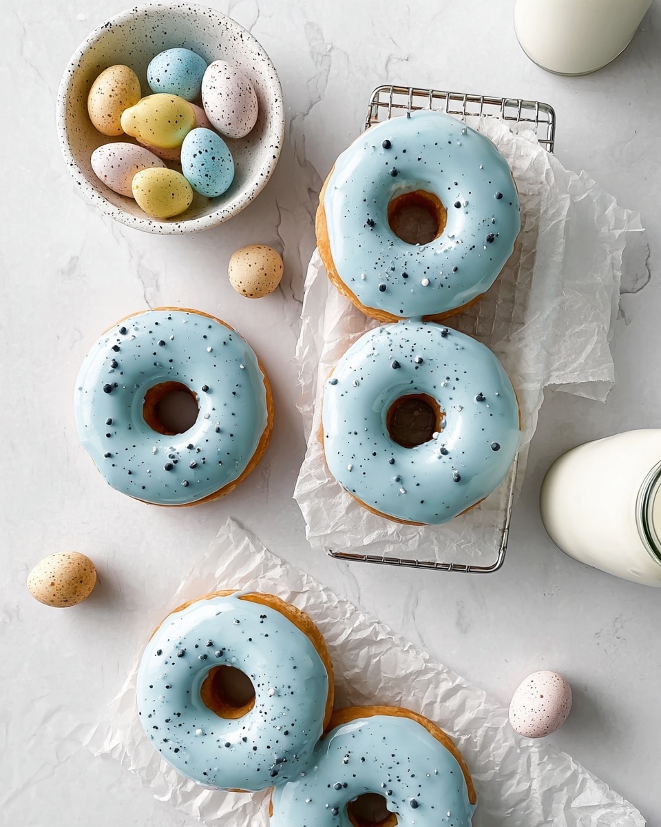 The image shows five donuts, each with a smooth light blue icing on top, decorated with small black speckles spread unevenly. The donuts have a golden brown base visible under the icing, giving a soft texture look. Three donuts are placed on white parchment paper on a small metal wire rack in the center, and the other two rest directly on a white marbled surface. In the upper left corner, there is a small white speckled bowl filled with pastel-colored mini eggs in yellow, white, pink, and blue. Scattered around the donuts are a few speckled mini eggs of white, beige, brown, and blue colors. A glass bottle of milk with a black rim is visible on the right side. The top-down composition is bright and clean, with the white marbled texture as the background to enhance the pastel colors. photo taken with an iphone --ar 4:5 --v 7