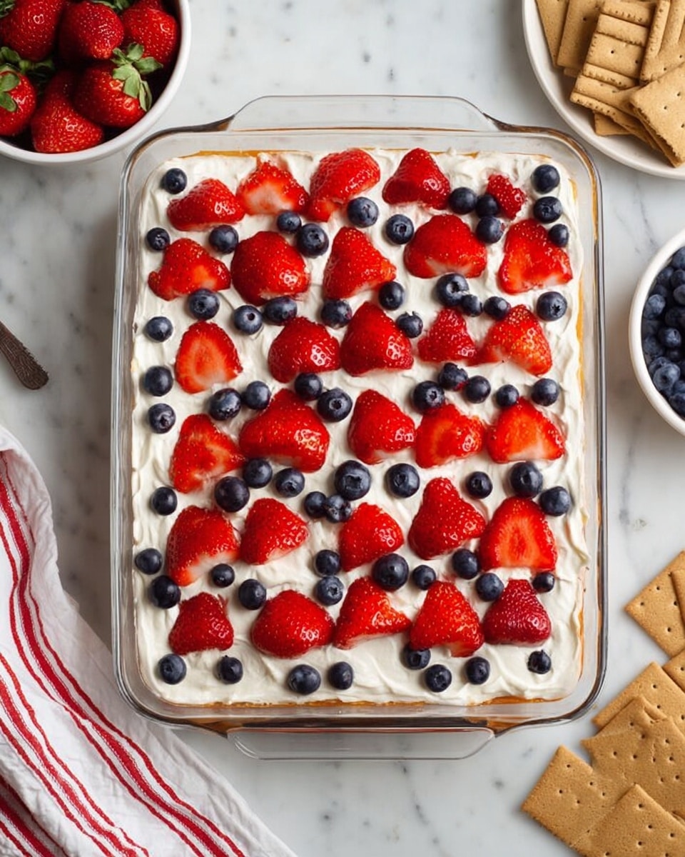 A clear rectangular glass baking dish with three visible layers: the bottom layer is light golden, the middle layer is creamy white and smooth, and the top layer is a thick white cream spread evenly across the dish. On top, whole small red strawberry halves are placed in rows covering the entire surface, with small dark blue blueberries scattered evenly between the strawberries. The dish is set on a white marbled surface, with a white bowl filled with strawberries and another with blueberries nearby, and some graham crackers in the top right corner. A white cloth with red stripes is partly visible in the bottom left corner. Photo taken with an iphone --ar 4:5 --v 7