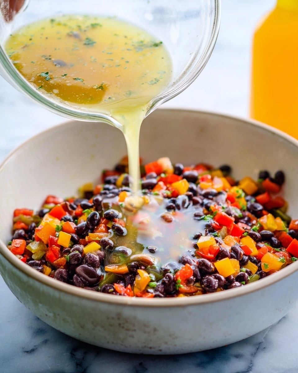 A white bowl filled with a colorful mix of black beans and diced red and yellow bell peppers with small bits of green herbs. A clear bowl above it is pouring a light yellow liquid dressing over the beans and peppers, creating a shiny layer on top. The background is a white marbled surface with a blurred yellow bottle in the back. The scene shows a woman's hand holding the clear bowl as the dressing flows smoothly into the bowl below. photo taken with an iphone --ar 4:5 --v 7