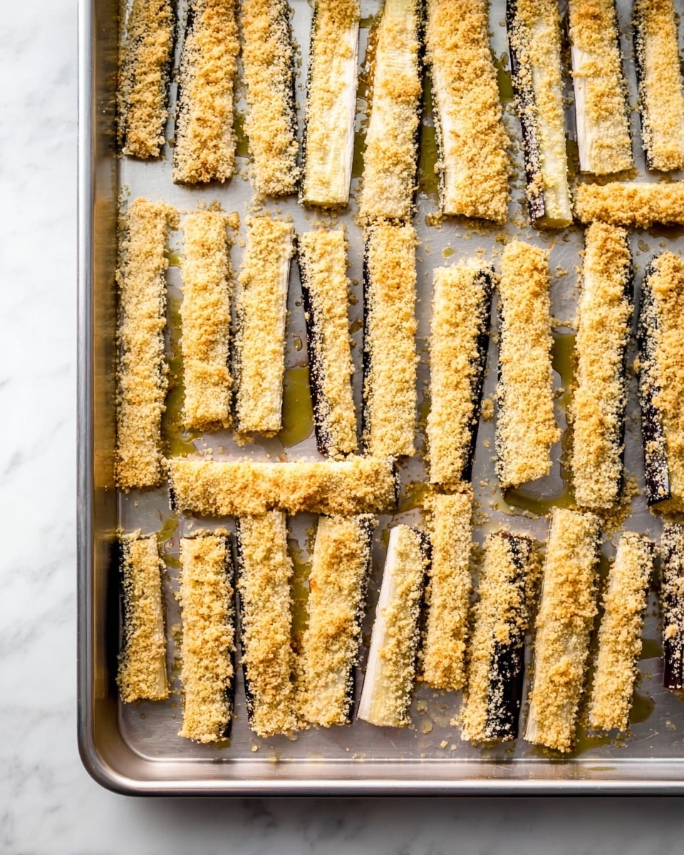 The image shows a silver baking sheet filled with many uncooked eggplant sticks evenly arranged in straight rows. Each stick is covered with a light, crumbly golden breadcrumb coating, giving a rough texture. The eggplant inside is purple and white, contrasting with the golden crumb layer. The baking sheet sits on a white marbled surface, and some light oil drizzles can be seen spreading under the eggplant sticks, giving a shiny look. Photo taken with an iphone --ar 4:5 --v 7