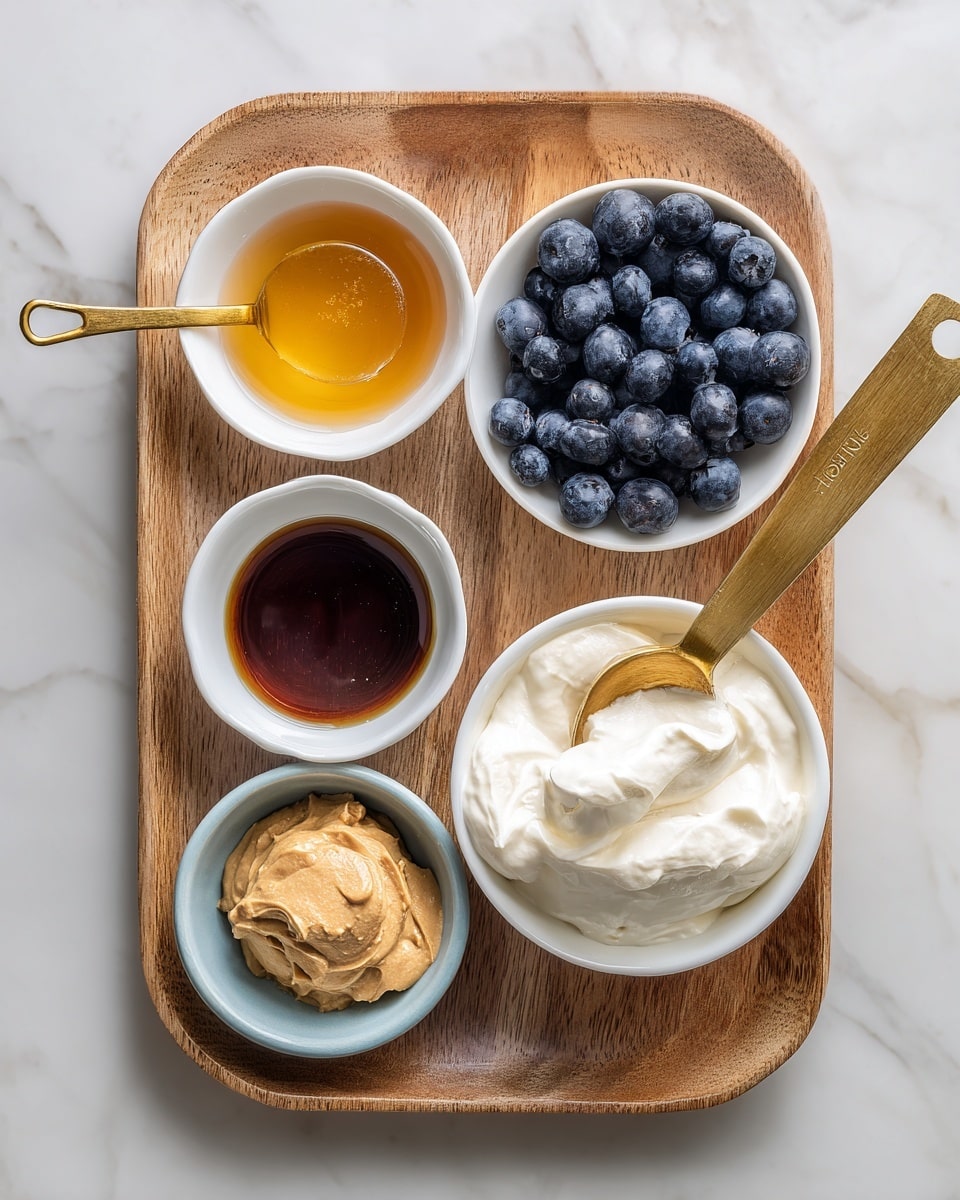 The image shows a wooden tray on a white marbled surface, holding five small dishes with different ingredients. Starting from the top left, there is a small white bowl filled with golden maple syrup. To the right, a measuring cup with a golden handle is full of dark blue, round blueberries. Below the syrup, a very small white bowl contains a dark amber vanilla liquid. Next to the vanilla is a light blue bowl with light brown powdered peanut butter. On the far right, a white bowl holds thick, creamy white Greek yogurt with a wooden spoon resting inside, with some yogurt on the spoon. Photo taken with an iphone --ar 4:5 --v 7
