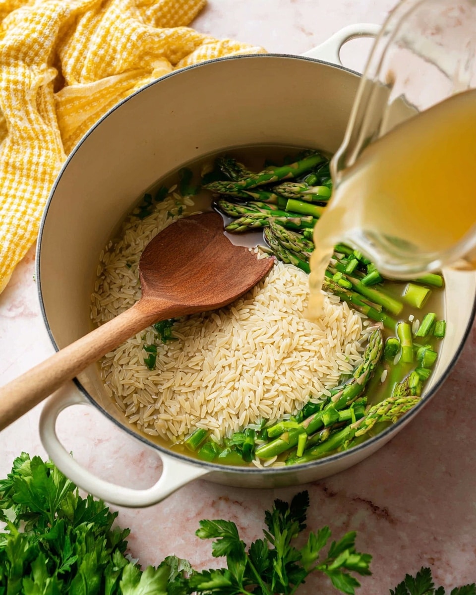 A white pot sits on a white marbled surface with chopped green asparagus pieces scattered around the bottom. On top of the asparagus lies a thick layer of raw orzo pasta, creamy beige in color with a grainy texture. A wooden spoon rests in the pot, pushing the orzo slightly to one side. Clear golden broth is being poured into the pot from a glass container on the right side. In the foreground, fresh green parsley is partially visible, adding a touch of green outside the pot. A yellow and white checkered cloth is placed nearby on the left. Photo taken with an iphone --ar 4:5 --v 7