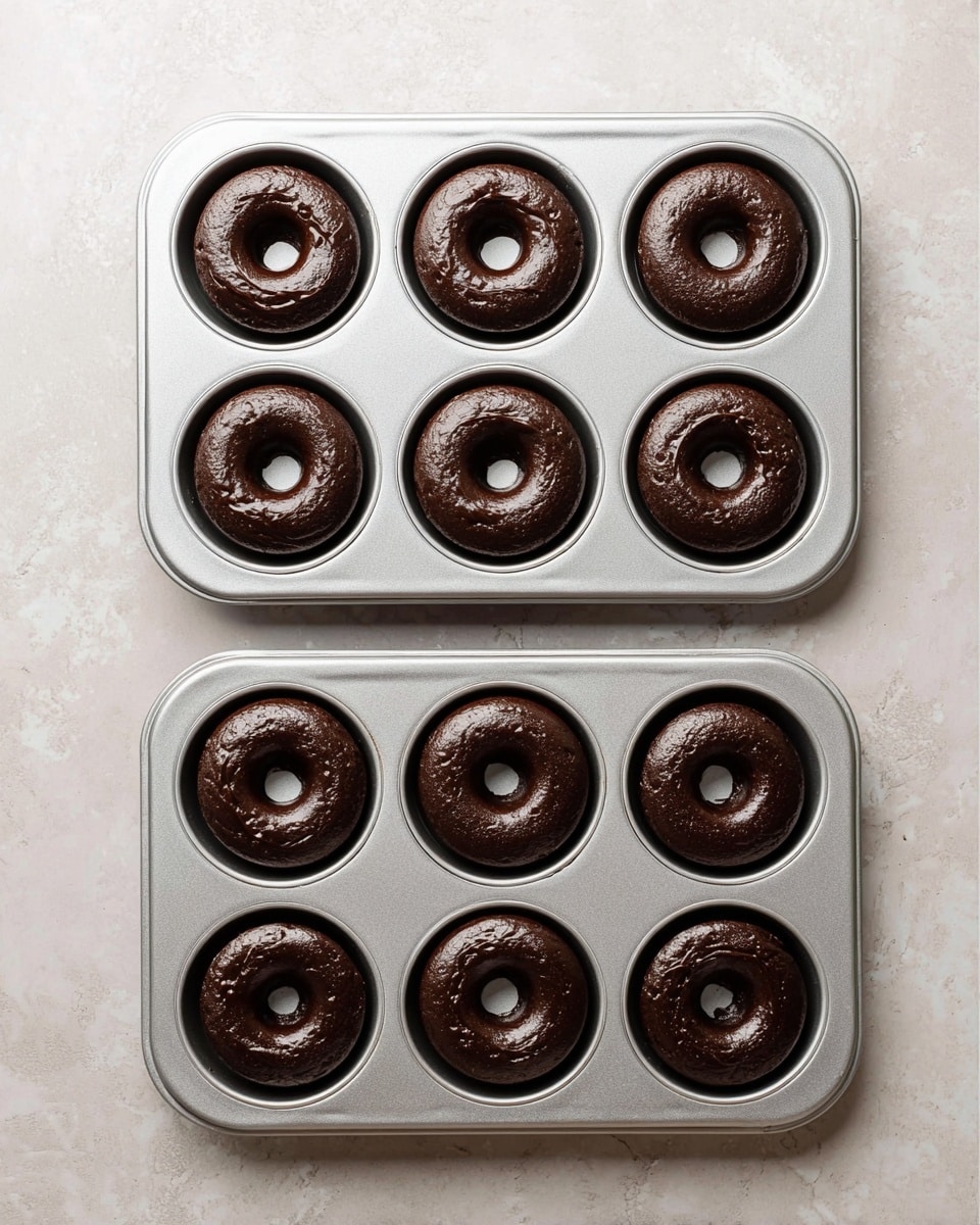 A group of dark chocolate donuts with a rough, slightly cracked texture are placed on a black wire cooling rack. The donuts are evenly spaced and show a rich, dense look with deep black color. The wire rack sits on a wooden surface with visible grain and rustic charm, creating a contrast with the dark donuts. There are multiple donuts lined up to cover most of the rack, each having a round shape with a central hole. Photo taken with an iphone --ar 4:5 --v 7