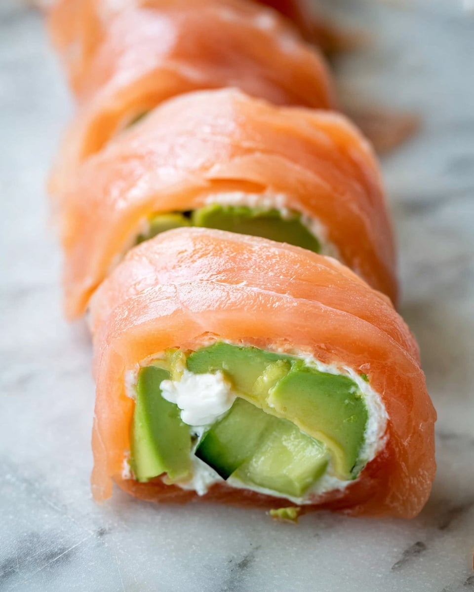 A close-up view of a roll made with a thin, translucent layer of light pink smoked salmon wrapped around a filling inside. The filling has a layer of bright green avocado with smooth texture, topped with small pieces of light green cucumber with a crisp appearance, and a small amount of white cream cheese spread is visible on the inside layer of the salmon. The roll is placed on a white marbled surface. photo taken with an iphone --ar 4:5 --v 7