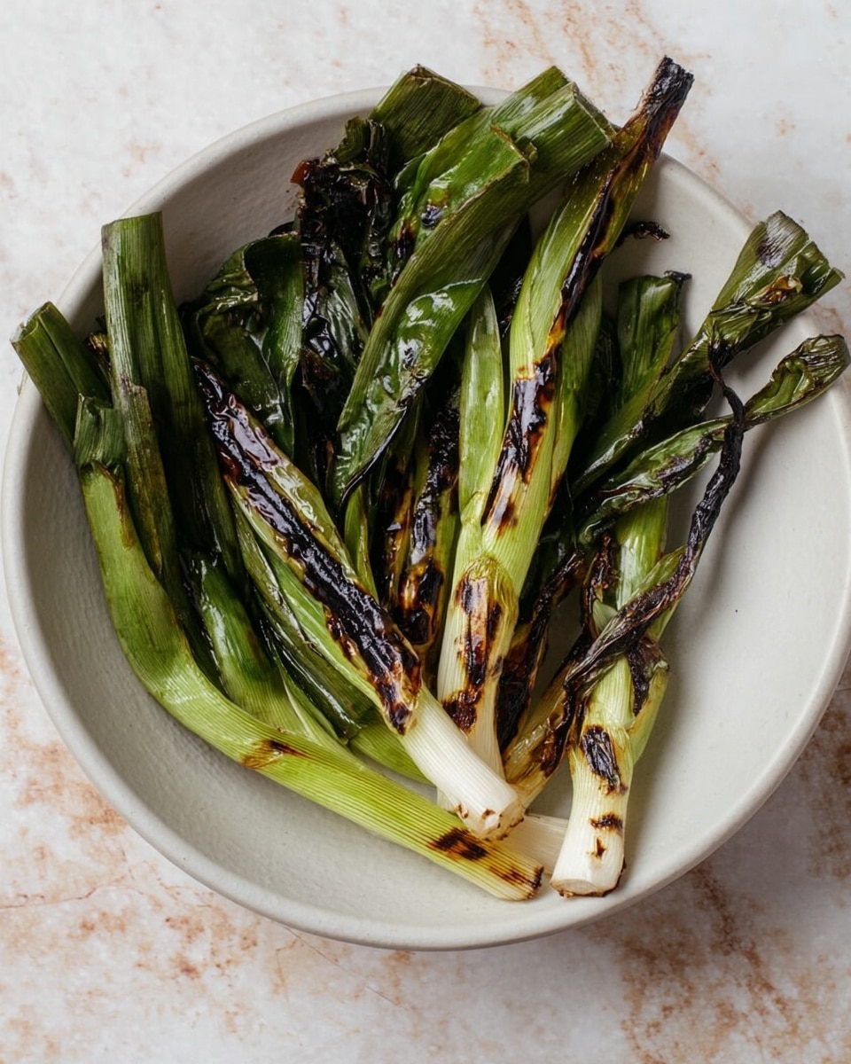A round white bowl holds grilled green onions arranged loosely in a curved shape around the edges, leaving the center empty. The onions show a mix of light green and white at the bulbs, with dark, charred marks on the longer green stalks, creating a rough texture. The bowl sits on a white marbled surface. photo taken with an iphone --ar 4:5 --v 7