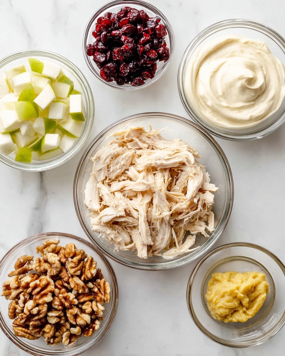 A top-down view of six clear glass bowls arranged on a white marbled surface, each filled with different ingredients. The largest bowl in the center contains light beige shredded chicken with a fibrous texture. At the top right, there is a bowl filled with smooth white mayonnaise. Above the chicken bowl is a small bowl of dark red dried cranberries, next to it on the left is a bowl with small white and green apple chunks. At the bottom left is a bowl filled with brown chopped walnuts, and to the far right is a very small bowl with yellow mustard. All bowls are transparent, showing the textures and colors clearly. Photo taken with an iphone --ar 4:5 --v 7