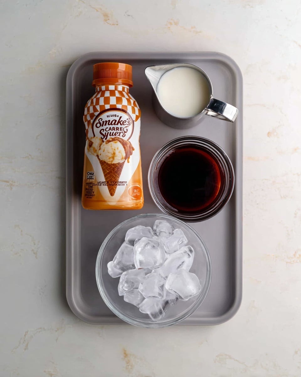 A light gray rectangular tray holds four items arranged neatly on a white marbled surface. At the bottom right corner of the tray is a round clear glass bowl filled with chunks of clear ice. Above it, on the right side, is a clear glass measuring cup filled with dark brown liquid. To the left of the measuring cup is a small metallic pitcher filled with white milk. On the left side of the tray is a plastic squeeze bottle of Smucker's Caramel Sundae Syrup with orange and white checkered pattern on the top half and caramel dripping over vanilla ice cream image on the lower half. The setup is viewed from above. Photo taken with an iphone --ar 4:5 --v 7