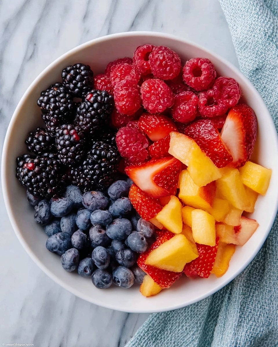 A white bowl filled with five distinct layers of fresh fruit placed side by side: black blackberries on the top left, bright red raspberries on the top center, dark blue blueberries on the top right, vibrant red strawberry pieces on the bottom left, and orange-yellow chunks of peach on the bottom right. The bowl is set on a white marbled surface with part of a light blue textured cloth visible to the right. The fruits are fresh and neatly arranged, showing rich and varied colors against the white bowl. photo taken with an iphone --ar 4:5 --v 7