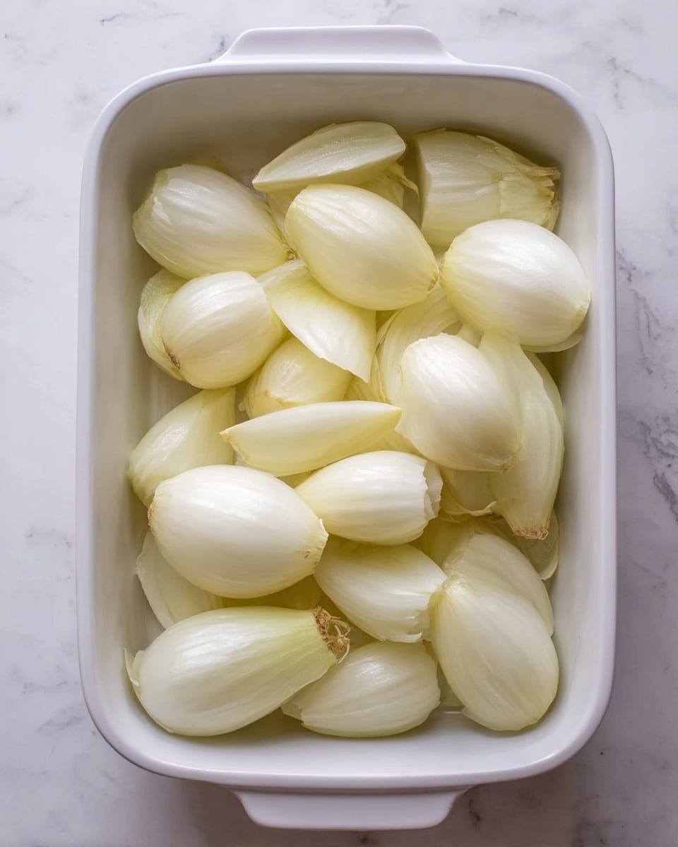 The left side shows a wooden board placed on a white marbled surface with peeled and hollowed onion layers arranged on it and in a white bowl, alongside a metal slotted spoon. The onion pieces are pale yellow and glossy with smooth texture. On the right side, a clear glass bowl contains a mix of raw minced meat combined with finely chopped herbs and onions, giving it a rough and chunky texture with red, green, and white colors. Surrounding the bowl on the white marbled surface are small dishes and containers holding dark sauce, raw rice, salt, and garlic cloves. The scene is bright and clean, emphasizing fresh ingredients. photo taken with an iphone --ar 4:5 --v 7