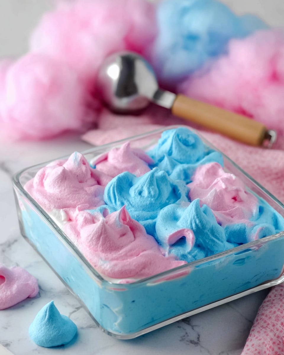 The image shows a close-up of a dessert in a glass square dish on a white marbled surface. The dessert has two layers of whipped cream or mousse: the bottom layer is bright blue, and on top, there are random dollops of blue and pink with a soft, fluffy texture and swirled peaks. In the background, there are fluffy pink and blue cotton candy piles that add a light, airy feel. A metal scoop with a wooden handle rests on the surface right behind the dish. The overall look is colorful, soft, and inviting. photo taken with an iphone --ar 4:5 --v 7