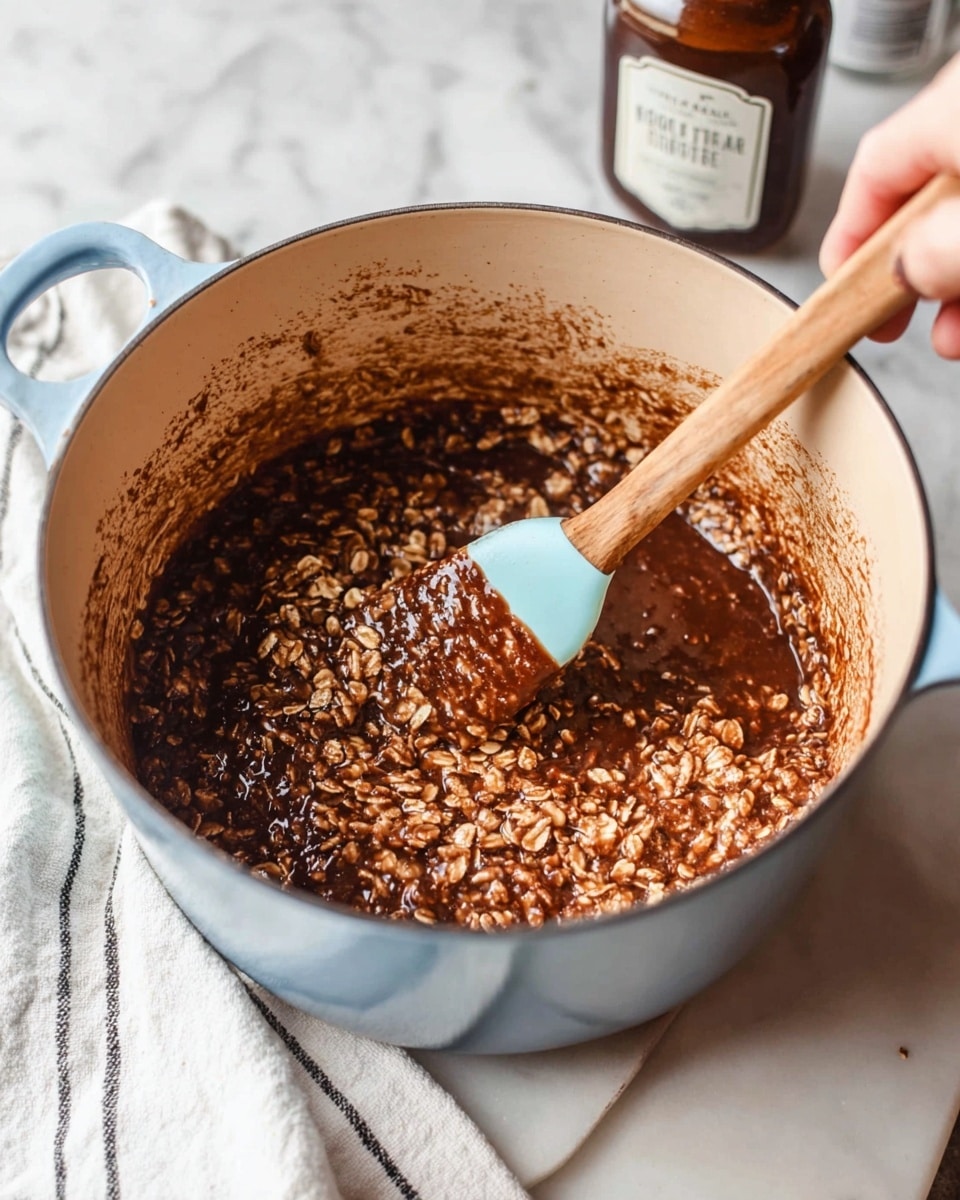 The image shows a light blue cast iron pot with a beige inside, filled with a mix of oats and thick, dark brown chocolate liquid. The mixture has a chunky texture with visible oats folded into the glossy chocolate base. A woman's hand holds a wooden spoon with a light blue silicone spatula head, stirring the mixture on the right side of the pot. Behind the pot, there is a brown bottle with a white label slightly blurred. The pot sits on a white marbled surface with a white cloth with black stripes at the bottom left corner. photo taken with an iphone --ar 4:5 --v 7