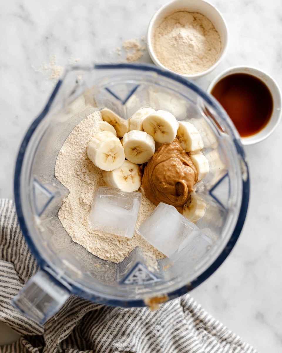 A clear blender jar filled with several layers: at the bottom, there is a light beige powder, on top of that are light yellow sliced bananas scattered around, with a dollop of creamy brown nut butter sitting on one side. Two large clear ice cubes rest near the center, with a small drizzle of dark brown liquid adding contrast near the ice and bananas. In the background, two small white bowls hold light beige powder and thick brown liquid, placed on a white marbled surface next to a folded gray and white striped cloth. photo taken with an iphone --ar 4:5 --v 7