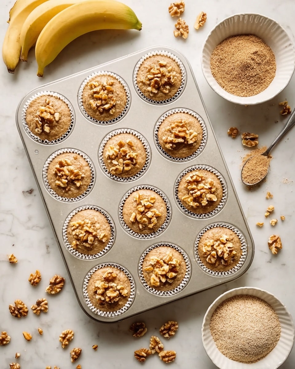 A white baking tray holds twelve unbaked muffins in white paper liners, each topped with small crunchy walnut pieces scattered over a light brown, grainy batter. The tray sits on a white marbled surface with some walnut pieces spread around. To the left, there are two ripe bananas, and near the top right corner, a small white bowl filled with a brown powdery ingredient, with some of it gently spilled around. Below it, another white bowl with a light brown grainy substance completes the scene, giving a soft and natural feeling to the whole setup. photo taken with an iphone --ar 4:5 --v 7