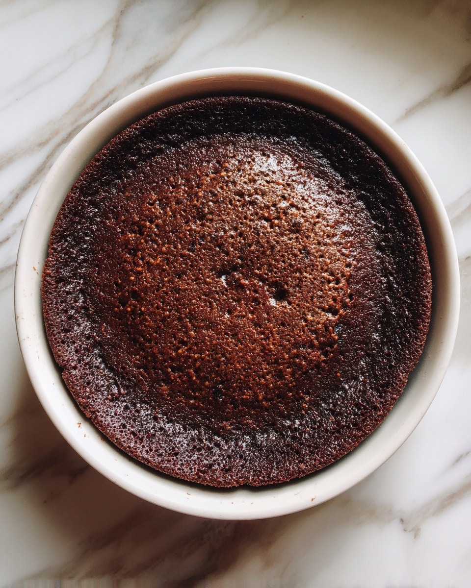 A round chocolate cake with one thick dark brown layer is shown inside a white ceramic round pan. The cake surface is slightly cracked, with a rough texture and some lighter brown dry spots. It sits on a white marbled surface. A white circle with the number 7 is visible in the top left corner. photo taken with an iphone --ar 4:5 --v 7