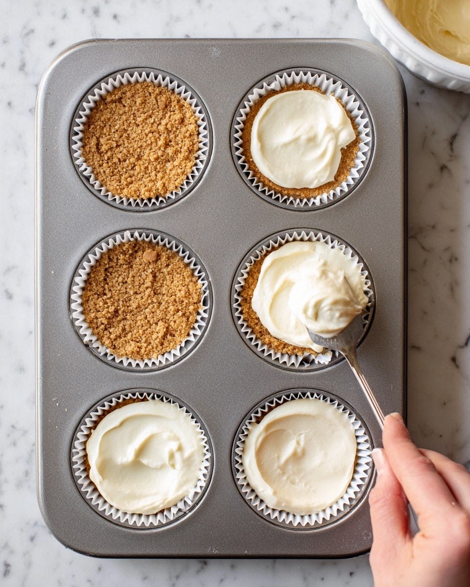 A silver muffin tray holds six white paper cups filled with layers of mini cheesecakes in progress. The top row has three cups with a crumbly, tan cookie base that looks rough and grainy. The middle right cup is being filled with a thick, creamy white layer, added with a spoon held by a woman’s hand coming from the right side. The bottom row shows three cups already topped with the smooth, creamy white filling, evenly spread over the tan base, creating two clear layers in each cup. The tray sits on a white marbled surface, and a large bowl with more of the creamy filling is partially visible in the top left corner. Photo taken with an iphone --ar 4:5 --v 7