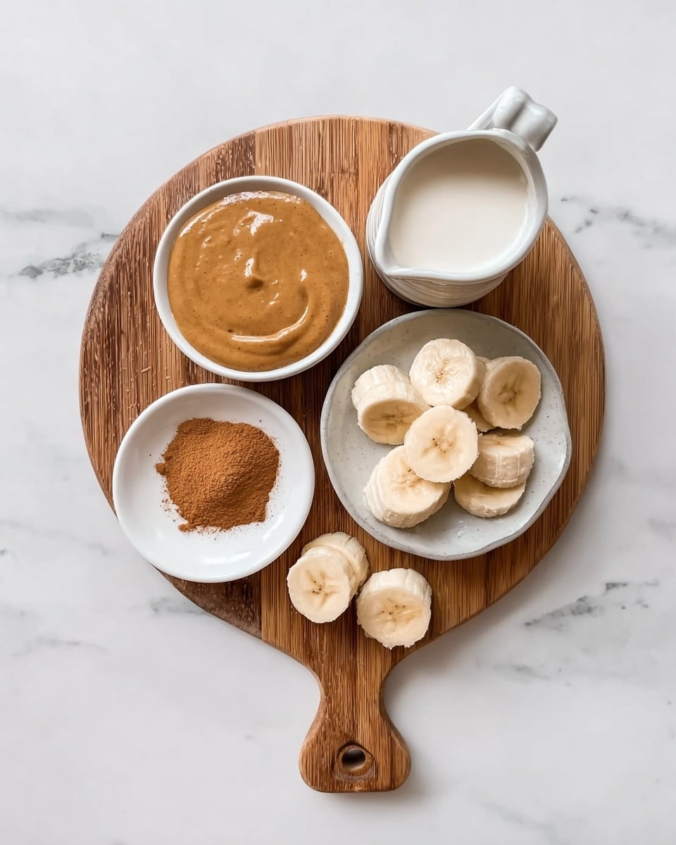 A round wooden board holds four small white dishes arranged in a loose square on a white marbled surface. The top left dish is filled with smooth, shiny peanut butter, light brown in color. To the right of it, a pitcher contains frothy white milk. Below the peanut butter, there is a small white plate with a mound of cinnamon powder in a warm brown tone. To the right of the cinnamon, a white bowl holds banana slices that are thick and creamy yellow with light brown centers. Two banana pieces lie on the wooden board handle in front of the bowl. Photo taken with an iphone --ar 4:5 --v 7