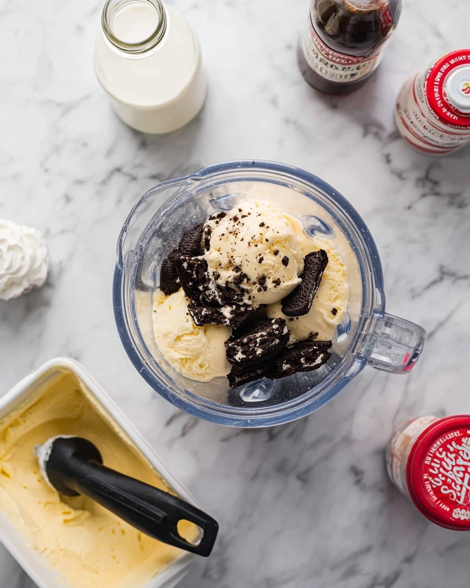 The image shows a clear blender container filled with broken dark chocolate sandwich cookies and scoops of pale yellow ice cream. The ice cream has a creamy, smooth texture with bits of cookie pieces on top. Surrounding the blender on a white marbled surface are a white tub of pale yellow ice cream with a black ice cream scoop resting in it, a small glass bottle filled with white milk, a bottle of dark brown chocolate syrup, and a bottle of red and white whipped cream. The scene is bright and clean with a focus on the ingredients before blending, photo taken with an iphone --ar 4:5 --v 7
