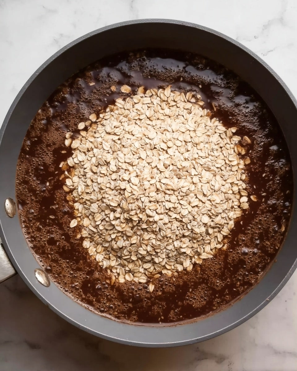The image shows a grey pan on a white marbled surface filled with a thick, dark brown liquid that is bubbling gently. In the middle of the pan, there is a large mound of light beige rolled oats sitting on top of the bubbling liquid, creating a noticeable contrast in color and texture. The oats appear dry and are layered evenly in the center, while the dark brown liquid looks smooth and slightly frothy around the edges. Photo taken with an iphone --ar 4:5 --v 7