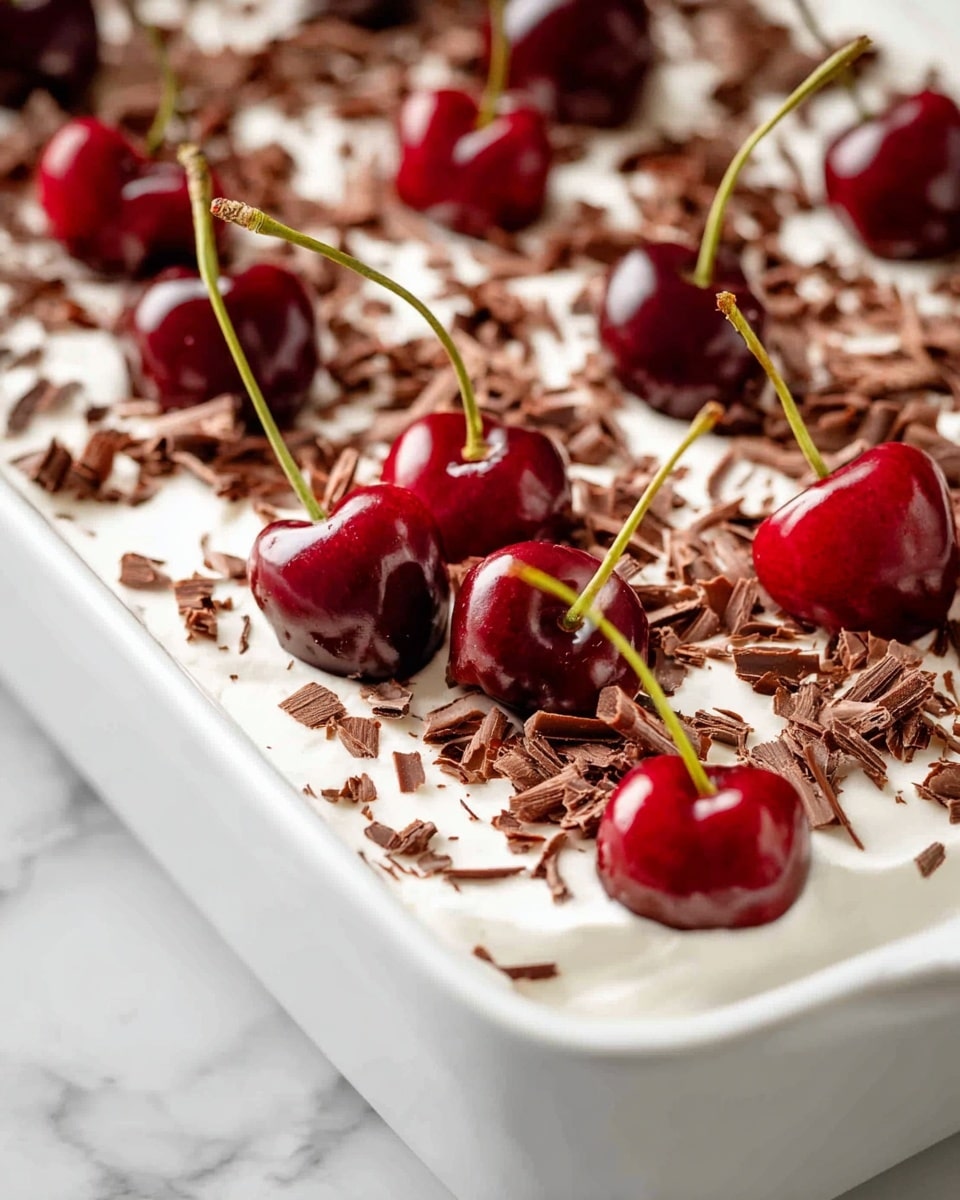 A white rectangular dish filled with one thick layer of smooth, white cream topped with scattered light brown chocolate shavings across the surface. On top of this layer, dark red cherries with their long green stems are evenly spread, some close to the front edge and others deeper inside, adding shiny, round shapes and bright contrast. The dish sits on a white marbled surface. photo taken with an iphone --ar 4:5 --v 7