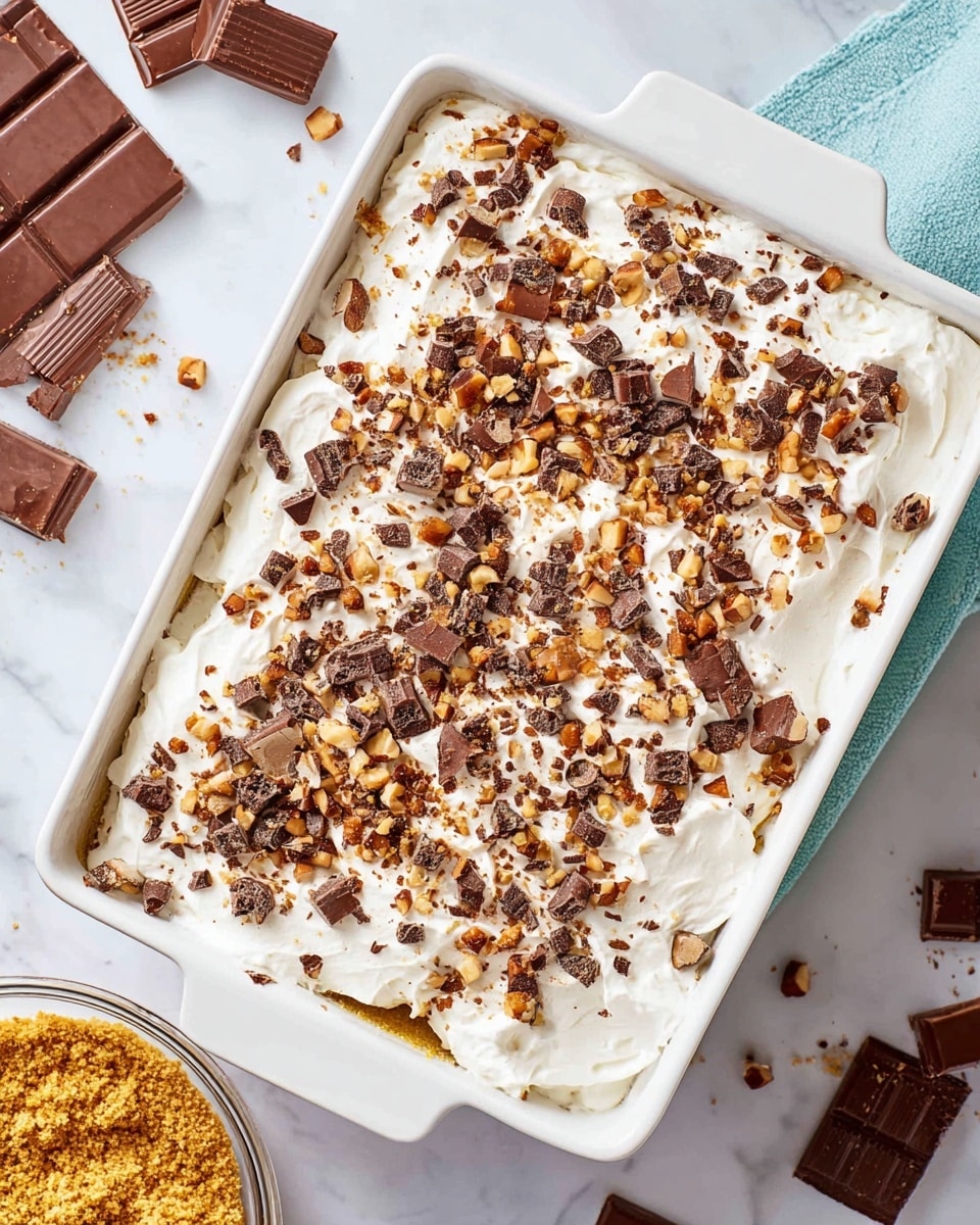 A white rectangular dish holds a dessert with three visible layers: the bottom crust is not fully visible but hints a golden color, the middle cream layer is thick and smooth with a pale off-white color, topped generously with fluffy, white whipped cream spread evenly. The whipped cream is heavily sprinkled with chopped chocolate pieces and small bits of nuts in brown and tan shades, adding texture and contrast. The dish is placed on a white marbled surface with broken chocolate bars and a clear round bowl filled with golden crumbs nearby, enhancing the visual appeal. The top right corner shows a small square piece slightly lifted, revealing the white cream layer inside, and the dish is cut into nine sections. Photo taken with an iphone --ar 4:5 --v 7
