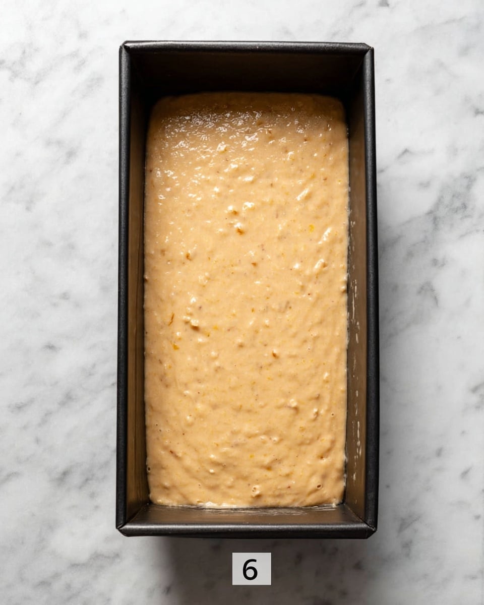 A rectangular black baking pan filled with smooth, light golden batter evenly spread inside, showing small bits of texture throughout the batter, placed on a white marbled surface, photo taken with an iphone --ar 4:5 --v 7
