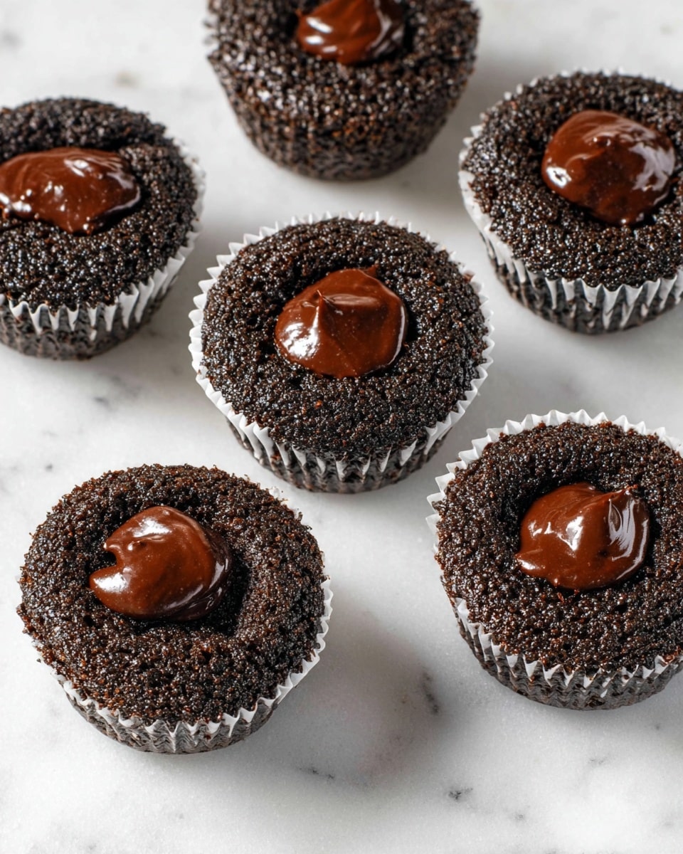 Five dark chocolate cupcakes sit scattered on a crinkled white parchment paper over a white marbled surface. Each cupcake has two layers visible: a rough, slightly cracked textured dark brown cake base forming the bottom layer, and a smooth, shiny dollop of thick chocolate filling resting in the center of the top layer. The cupcakes are all in white paper liners that hug their edges tightly. photo taken with an iphone --ar 4:5 --v 7