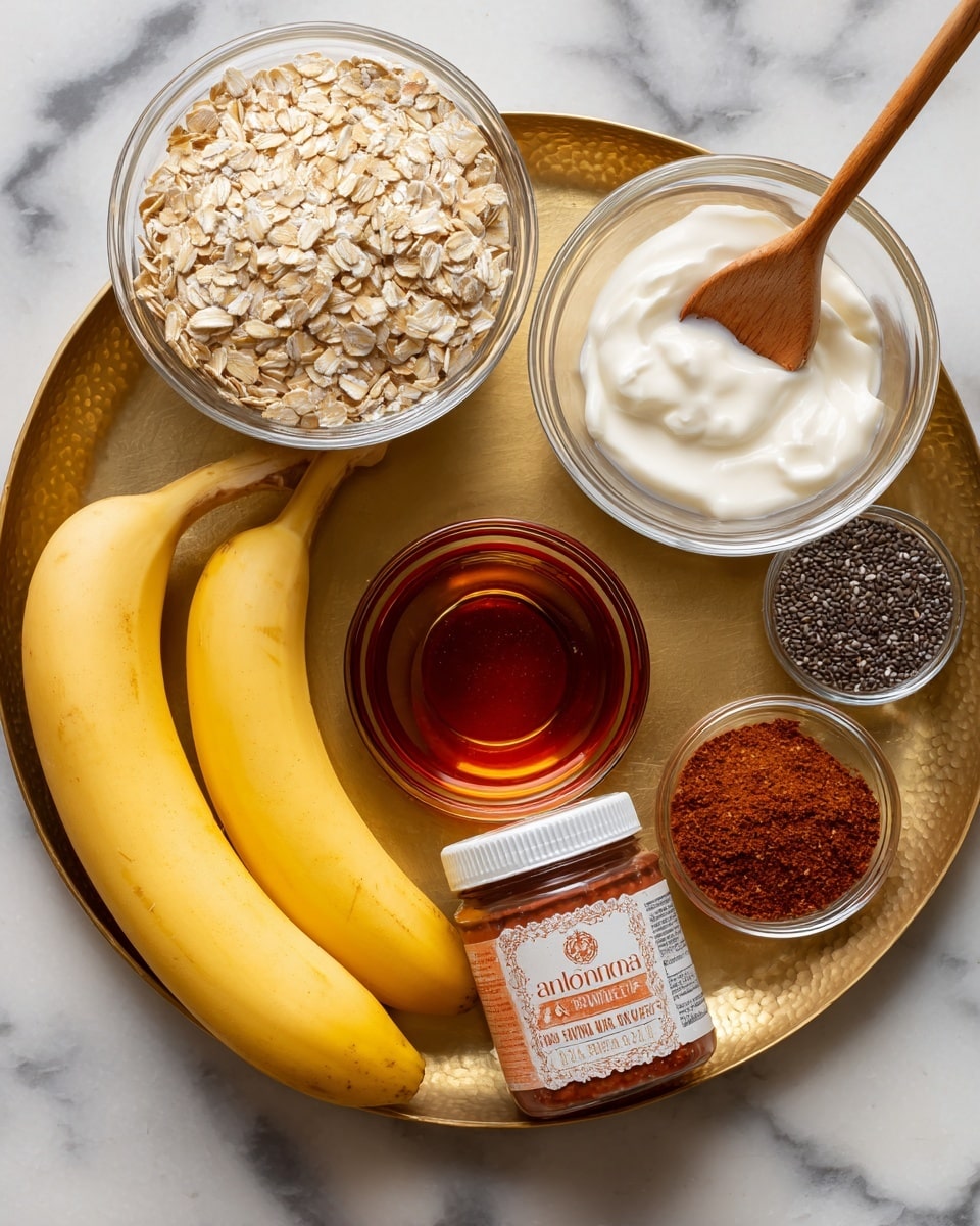A tray with a golden surface holds several ingredients for a recipe. In the top left, there is a clear glass bowl filled with light beige old fashioned oats. To the right, another clear glass bowl contains white yogurt with a wooden spoon inside. Below the oats, a small clear glass bowl has a dark amber liquid labeled as maple syrup or honey. In the center of the tray, there is a jar of cinnamon almond butter with a white lid and orange and red text. At the bottom left, two whole yellow bananas lie on the tray. Near the bananas and almond butter, a small clear glass bowl holds black chia seeds, and next to it is another small clear bowl filled with reddish-brown cinnamon powder. A silver measuring spoon rests nearby. The background is a white marbled texture. photo taken with an iphone --ar 4:5 --v 7