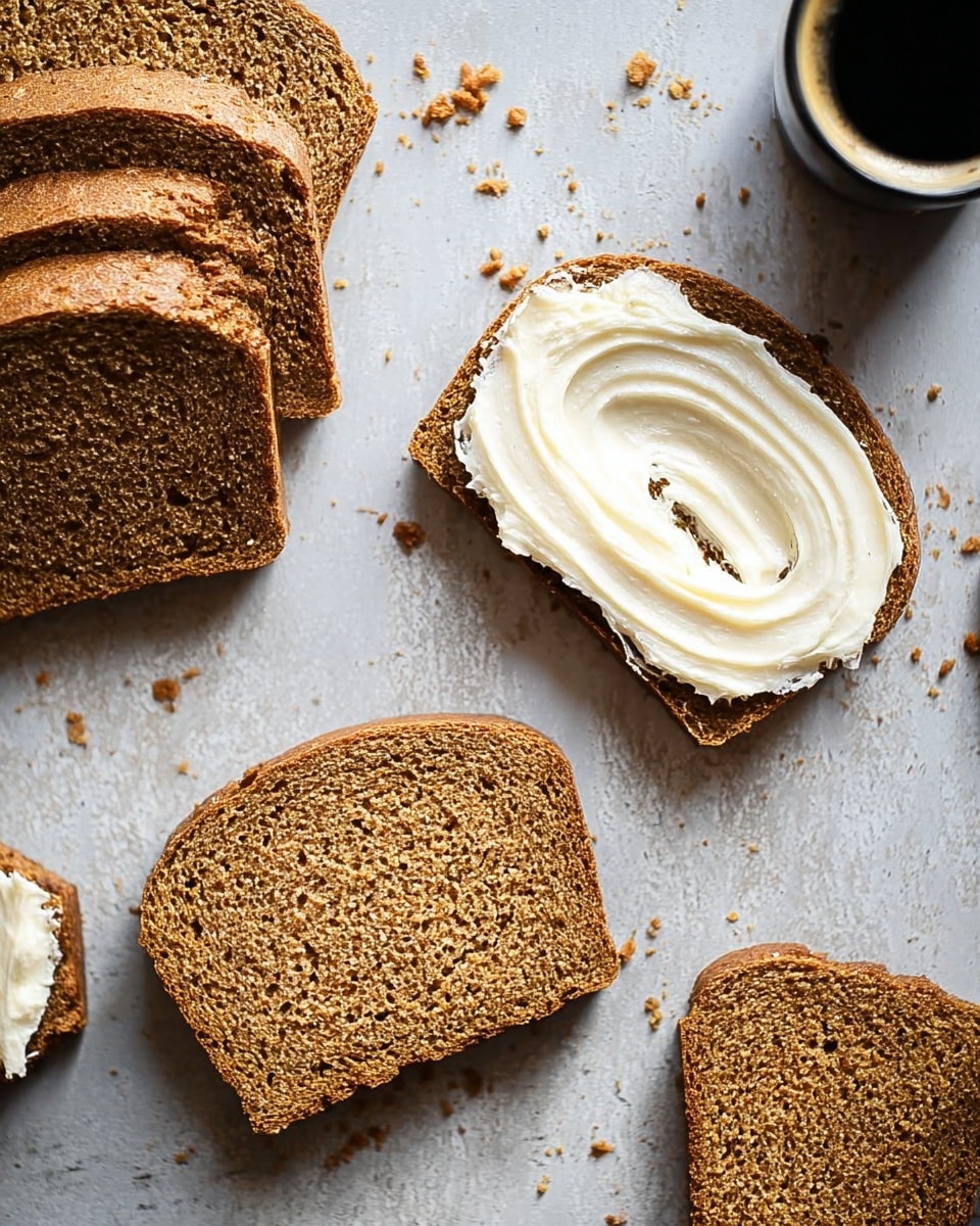 The image shows five slices of brown bread arranged on a light gray, slightly textured surface with some crumbs scattered around. Four whole slices are stacked on the left side, while one slice lies flat on the right with a thick layer of white, creamy spread smoothly swirled on top. Next to this slice, a small piece of bread with a smaller amount of spread sits close by. In the top right corner, a dark-colored cup filled with coffee or dark liquid is partially visible. The overall scene has a simple, clean look with natural light. photo taken with an iphone --ar 4:5 --v 7