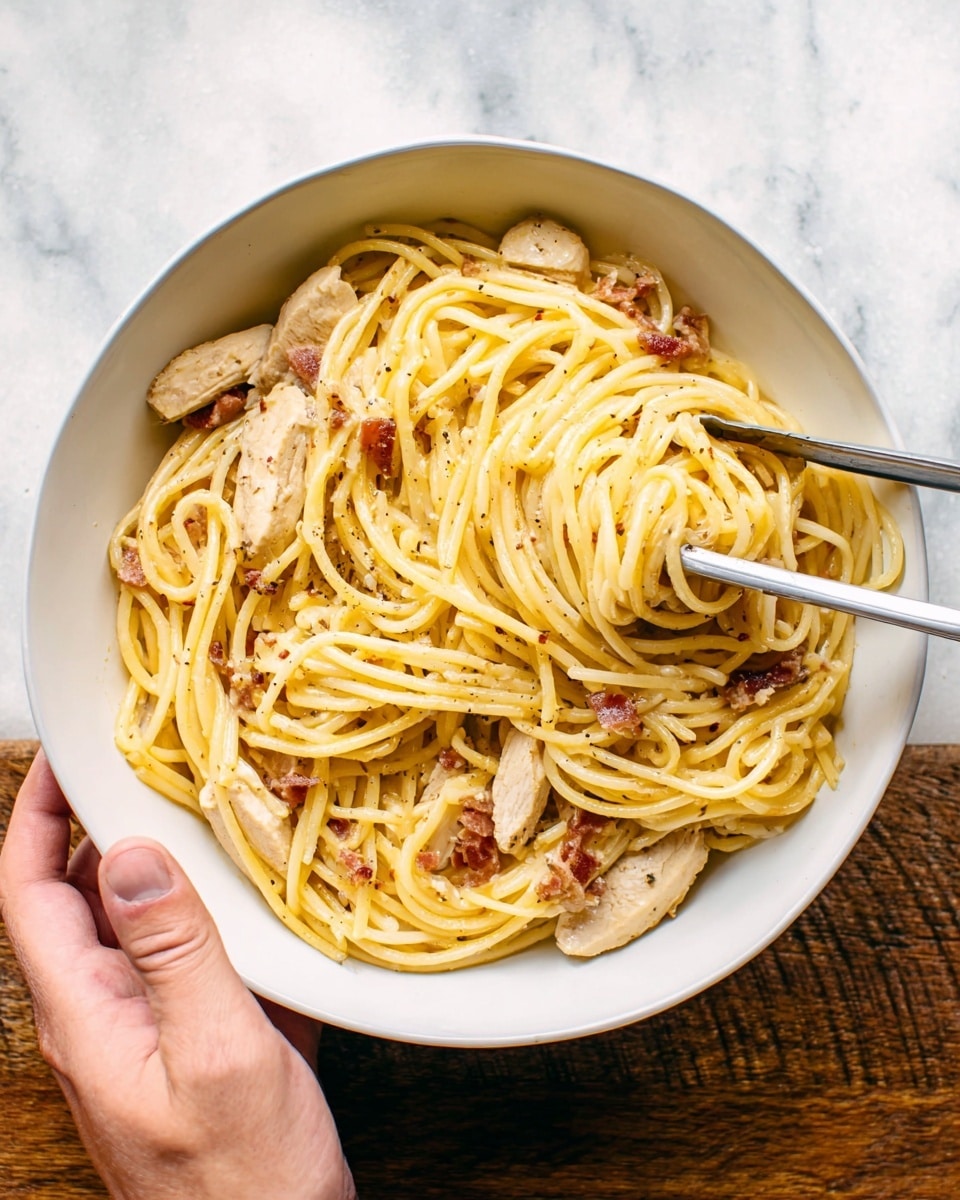 A white bowl filled with thick spaghetti pasta that is golden yellow in color, mixed with light beige slices of chicken, and small pieces of browned bacon spread unevenly throughout. Two metal tongs rest in the bowl on one side, partially buried in the noodles. A woman's hand is holding the side of the bowl, which sits on a white marbled textured surface. photo taken with an iphone --ar 4:5 --v 7