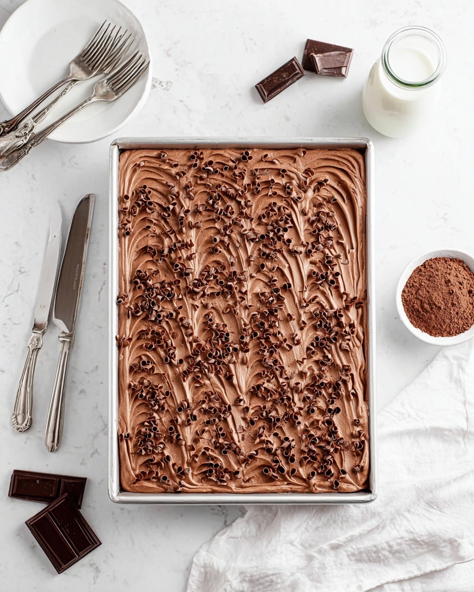 A rectangular metal tray filled with a thick, smooth chocolate mousse layer topped with small, loose chocolate curls evenly spread across the surface. The mousse has a rich brown color with soft, wavy textures made by a spreading tool. The tray sits on a white marbled surface, with a small white bowl of cocoa powder and a tall glass bottle of milk nearby. In the top left corner, a white plate holds two silver forks, and at the bottom left are three pieces of dark chocolate. A silver knife rests near the bottom right corner with a white cloth underneath. photo taken with an iphone --ar 4:5 --v 7