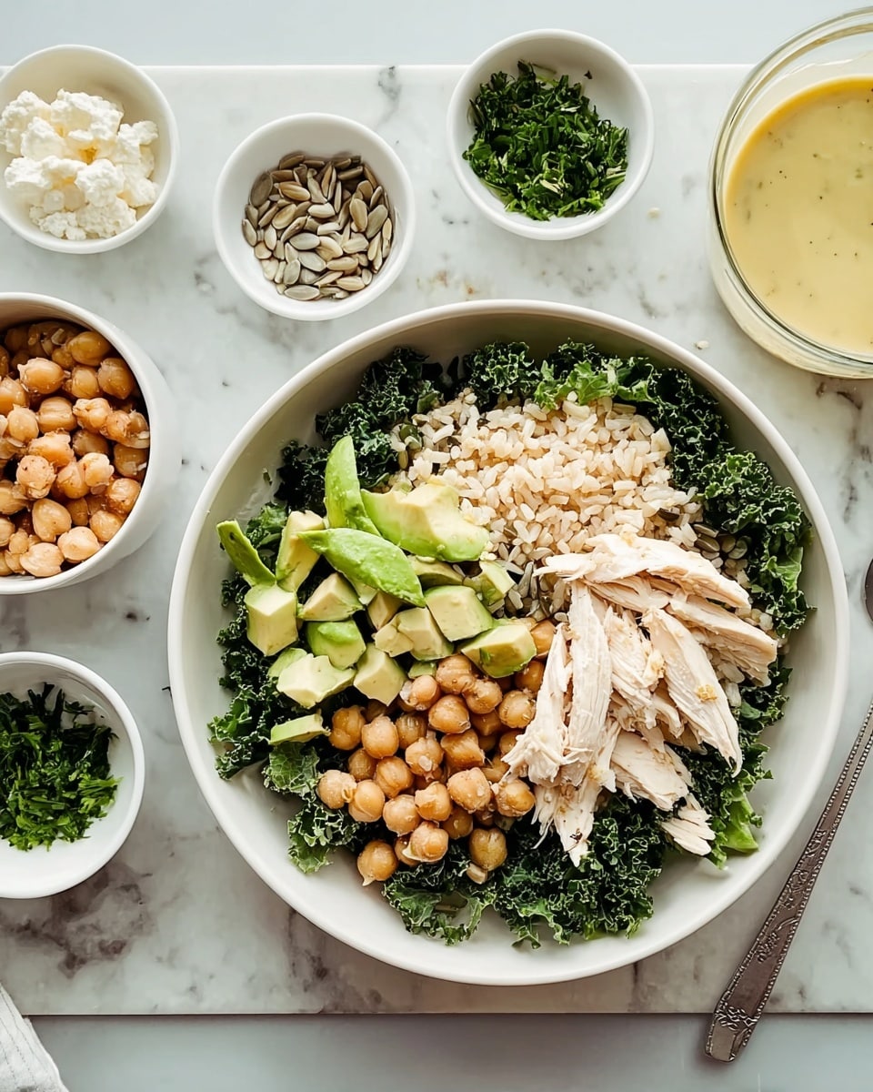 A white bowl sits on a white marbled surface and is filled with several layers: at the bottom is a layer of light brown rice covering most of the bowl, topped with dark green curly kale leaves scattered evenly. On top of the kale are small, light brown roasted chickpeas and medium-sized chunks of light green avocado. Several strips of light beige shredded chicken are layered on the top center. Around the bowl, there are small white bowls holding extras like sunflower seeds, more roasted chickpeas, finely chopped green herbs, cottage cheese, and a glass bowl of light yellow sauce with a white spoon. photo taken with an iphone --ar 4:5 --v 7