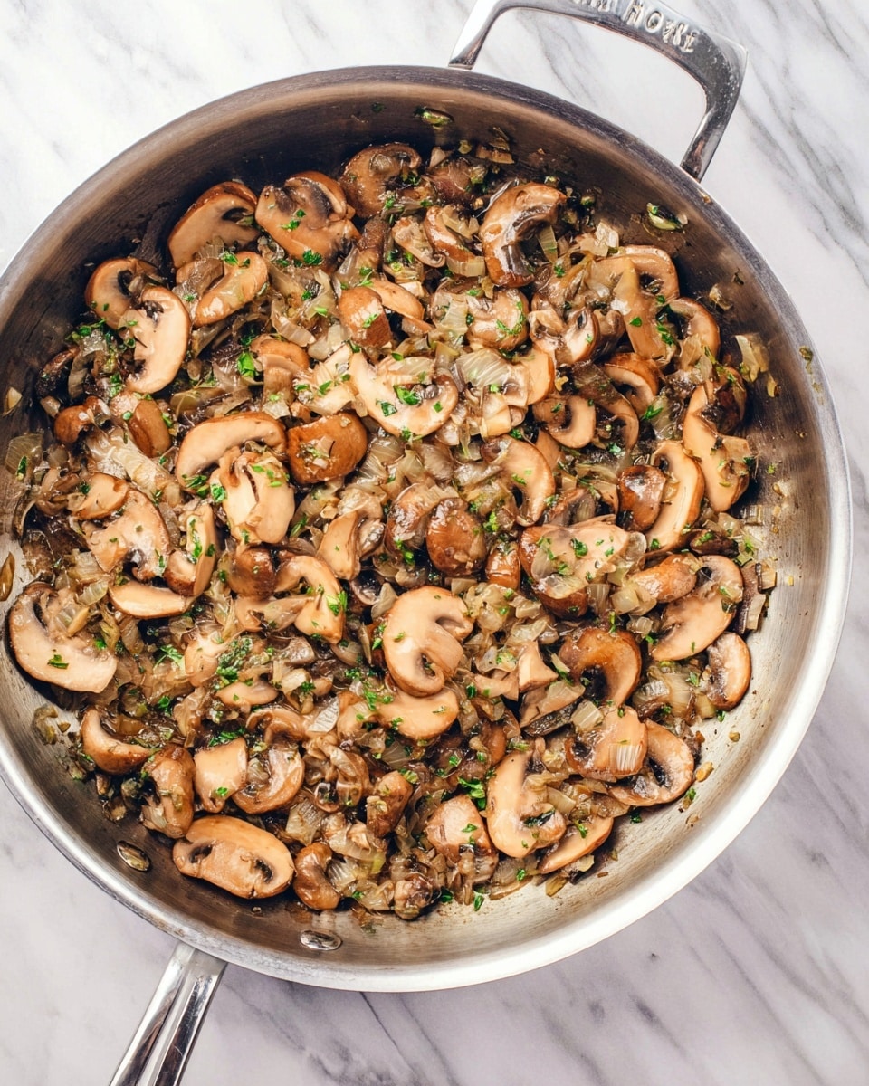 A shiny silver pan filled with cooked sliced mushrooms mixed with small pieces of cooked onions and herbs, all showing a soft, slightly shiny texture in brown and beige tones with hints of green from herbs, placed on a white marbled surface. photo taken with an iphone --ar 4:5 --v 7