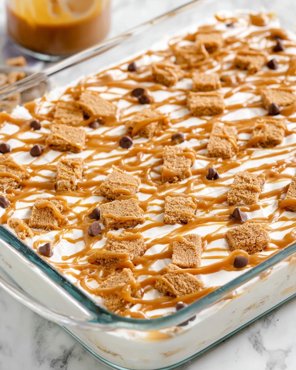 A clear glass baking dish filled with a layered dessert, starting with a smooth, creamy white base layer. On top, scattered pieces of light brown, crunchy cookies create a rough textured second layer. Above the cookies is a drizzle of thick caramel-colored sauce, forming a crisscross pattern that spreads unevenly and some sauce pools around cookie pieces. Small caramel-colored chocolate chips are also scattered across the surface, adding extra texture and color contrast. The dish sits on a white marbled surface with a blurred caramel sauce container in the background. photo taken with an iphone --ar 4:5 --v 7
