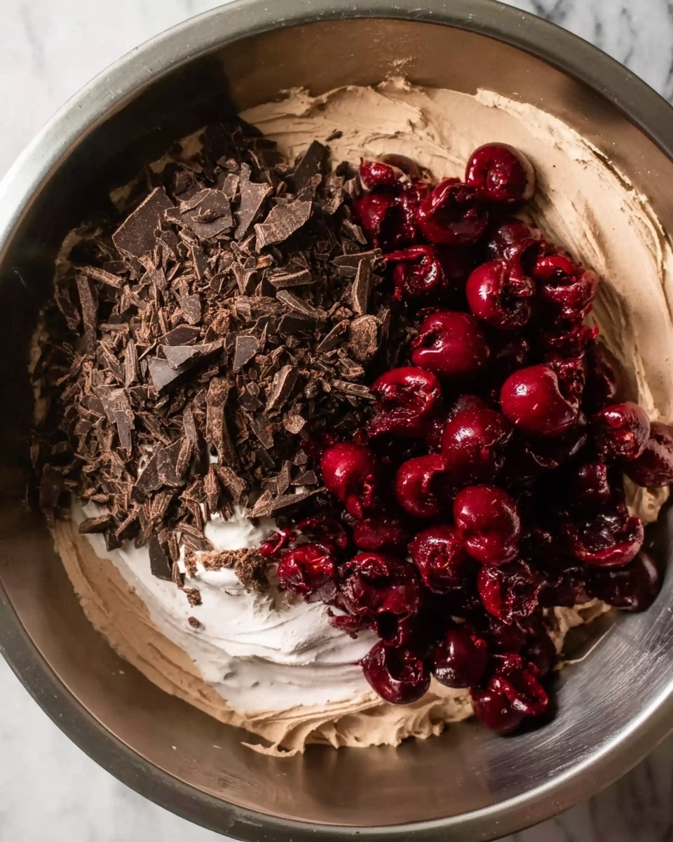 In this image, there is a large metal bowl filled with a light brown creamy mixture as the base layer, creating a smooth and soft texture. On one side of the bowl, there is a pile of dark chocolate pieces, roughly chopped, with their jagged edges and uneven shapes adding a rough texture. Next to the chocolate, there is a heap of dark red cherries with a shiny, slightly wet surface, some whole and some with exposed inner flesh. The three layers – light brown cream at the bottom, dark chocolate pieces, and deep red cherries – sit closely together inside the bowl, inviting a mix of flavors. The background shows a white marbled texture. Photo taken with an iphone --ar 4:5 --v 7