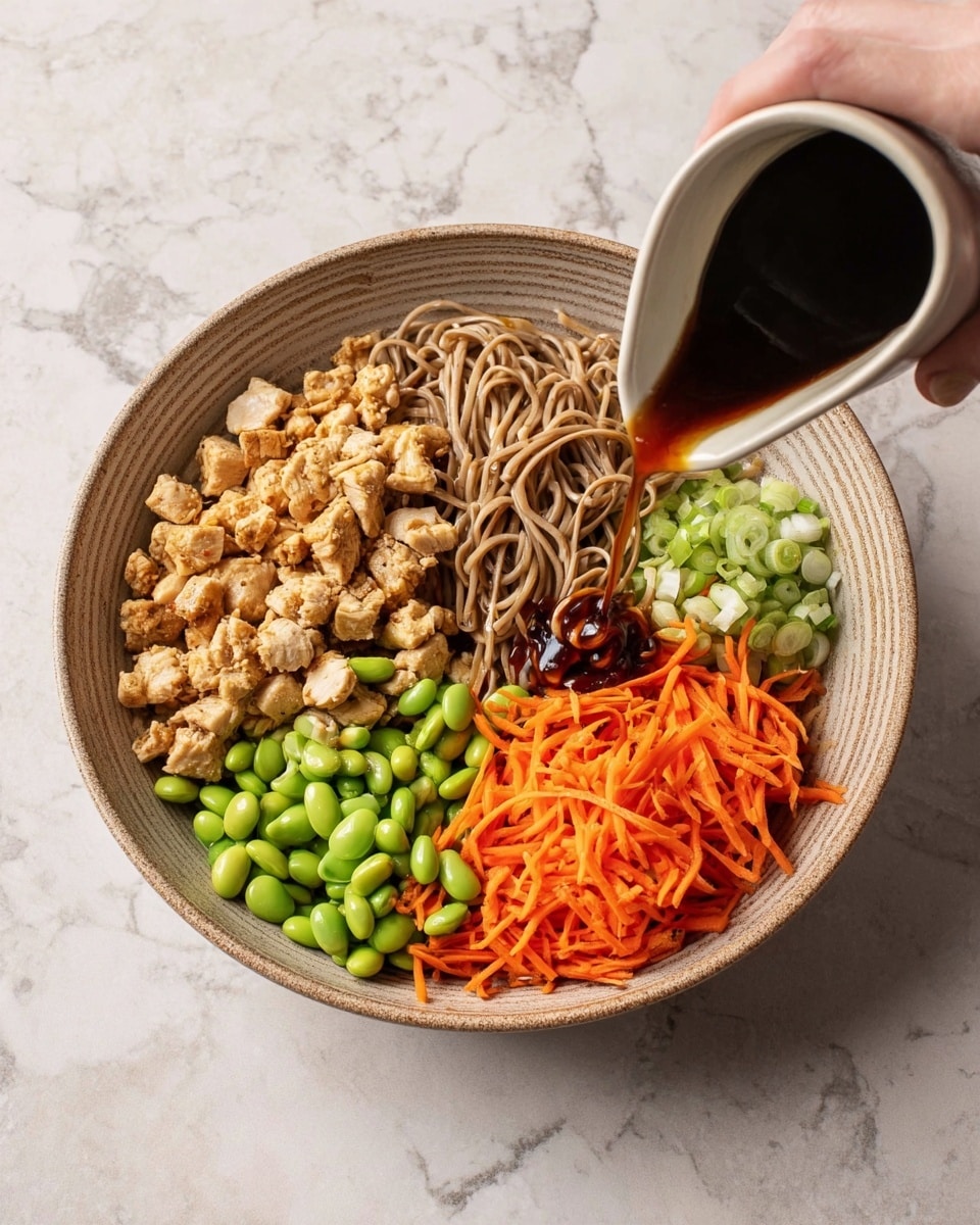 A round bowl filled with four main layers arranged side by side: on the left, small pieces of cooked light brown chicken, next to it a pile of light brown noodles, on the right side, bright orange shredded carrots, and below the carrots, sliced light green scallions; in the upper middle, a cluster of green edamame beans. A woman's hand is pouring a dark brown sauce over the ingredients. The bowl sits on a white marbled surface. photo taken with an iphone --ar 4:5 --v 7