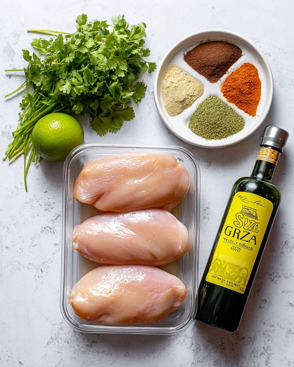 The image shows three raw pale pink chicken breasts placed side by side in a clear container at the center on a white marbled surface. Above them to the right is a white bowl with five different powders in sections: dark brown, greenish yellow, bright reddish-orange, beige, and a light green herb. To the left of the chicken breasts is a whole green lime, and next to it is a dark green bottle with a bright yellow label that reads