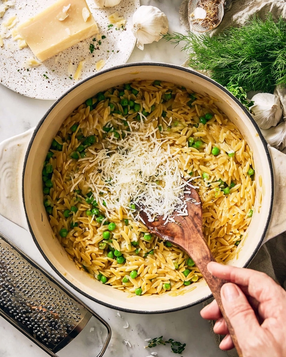 A white pot filled with cooked orzo pasta mixed with bright green peas makes up the main dish, with a woman's hand sprinkling a small pile of shredded white cheese over the top. The orzo is yellowish and glossy, evenly mixed with the peas. A wooden spoon is stirring the pasta and cheese together in the pot. On the white marbled surface around the pot, there is a head of garlic, green herbs, and a white speckled plate with a block of hard cheese and more shredded cheese next to a metal grater. Photo taken with an iphone --ar 4:5 --v 7