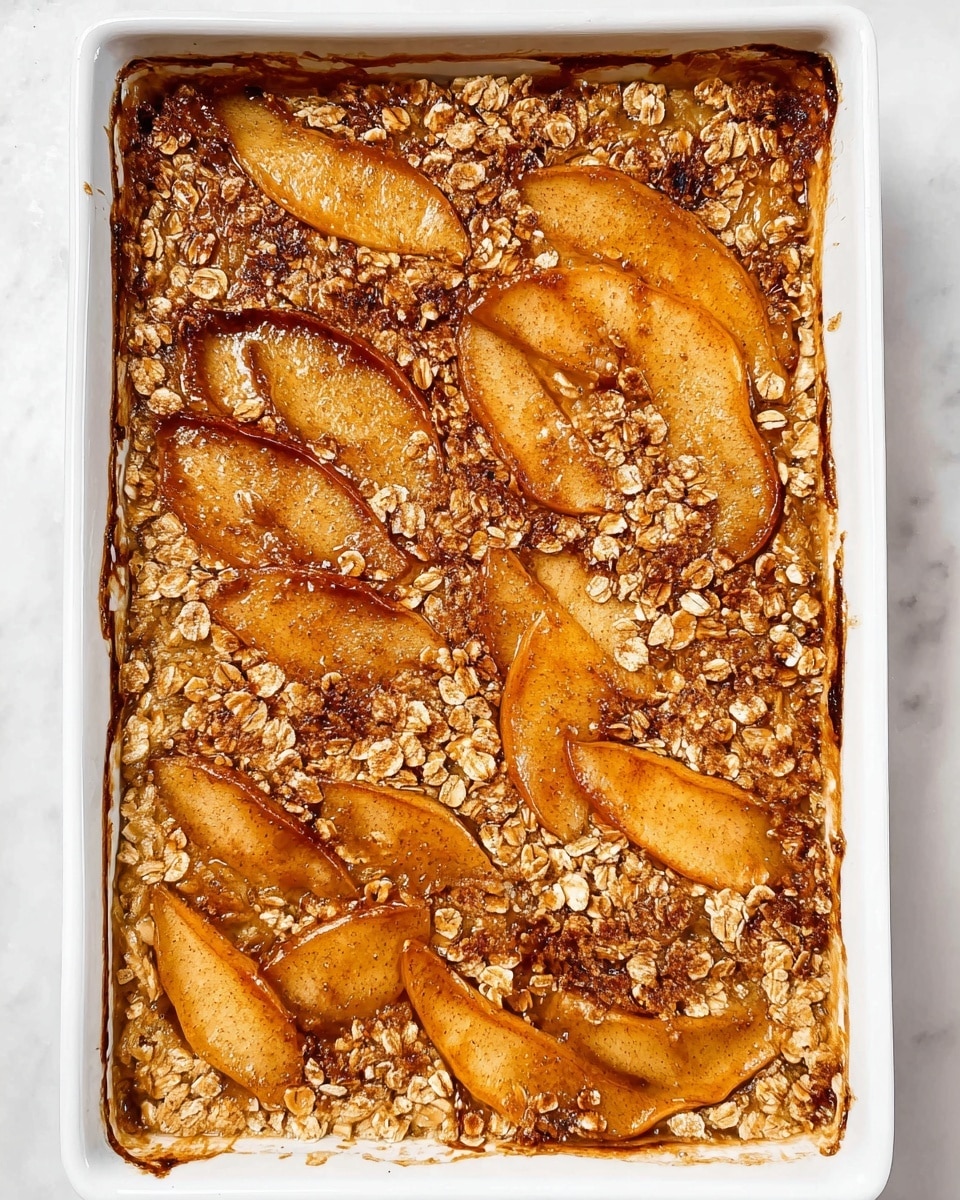 A rectangular white dish filled with a baked dessert that has a golden-brown top layer made of thin slices of fruit, likely apples or pears, arranged overlapping inside. The fruit is covered with a sprinkle of oats and a cinnamon-colored powder spread evenly across the surface, giving a textured look. The edges of the fruit slices are browned slightly, showing a warm cooked texture. The white dish rests on a white marbled surface. photo taken with an iphone --ar 4:5 --v 7