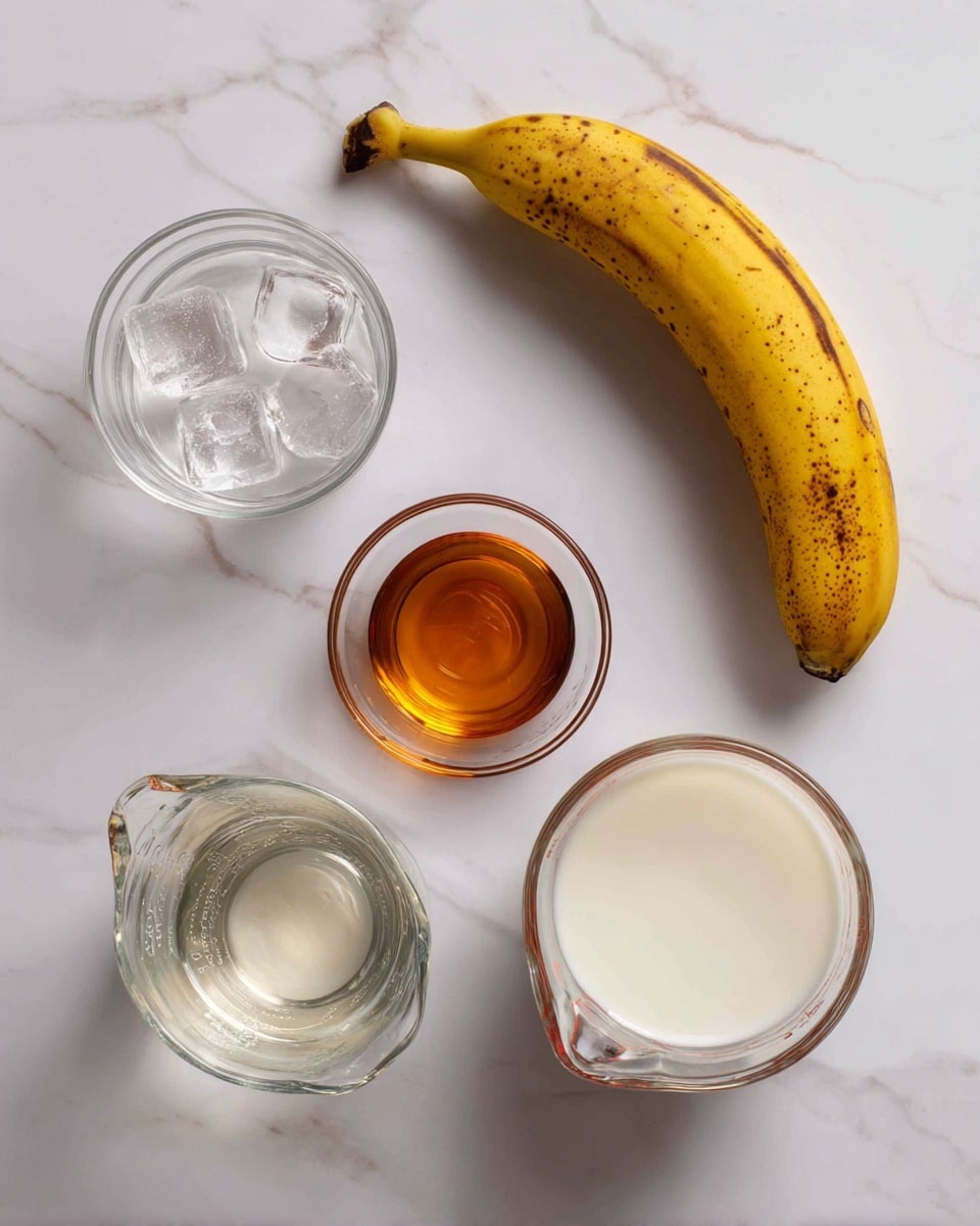 A yellow banana with brown spots is placed near the top center of a white marbled surface. Below it, there are four glass containers arranged in a loose square: a small clear bowl with ice cubes on the left, a small clear bowl with a bit of amber-colored vanilla liquid on the right, a glass measuring cup with cold water in the bottom left, and a larger glass measuring cup filled with white milk in the bottom right. Each ingredient is labeled with simple black text above or beside it. photo taken with an iphone --ar 4:5 --v 7