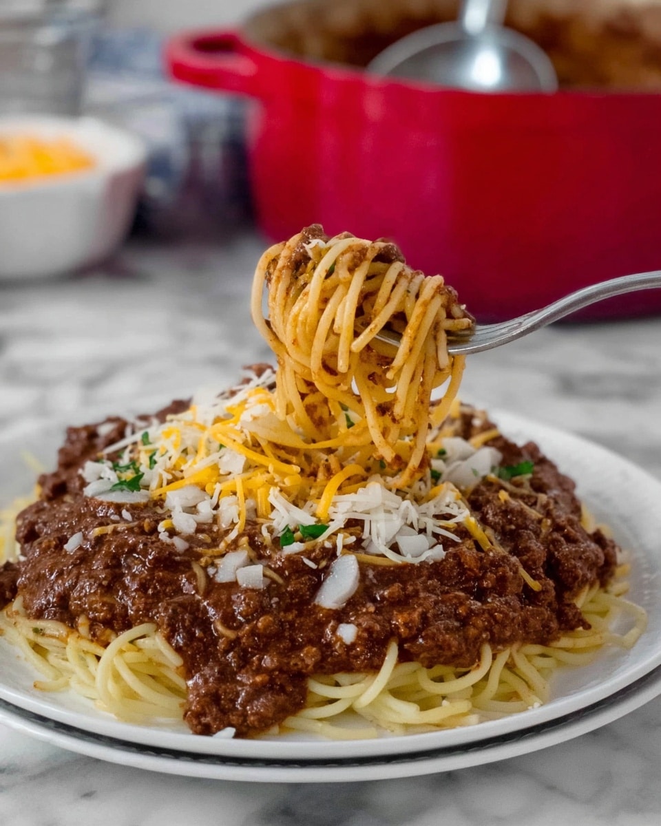 A white plate holds a serving of spaghetti with a thick layer of dark brown meat sauce spread on top. On this, there are scattered shredded cheeses in yellow and white, along with small bits of chopped white onion. A fork lifts a twisted bundle of spaghetti mixed with meat sauce from the plate. The background shows a red pot with a silver ladle and a white bowl, all on a white marbled surface. photo taken with an iphone --ar 4:5 --v 7