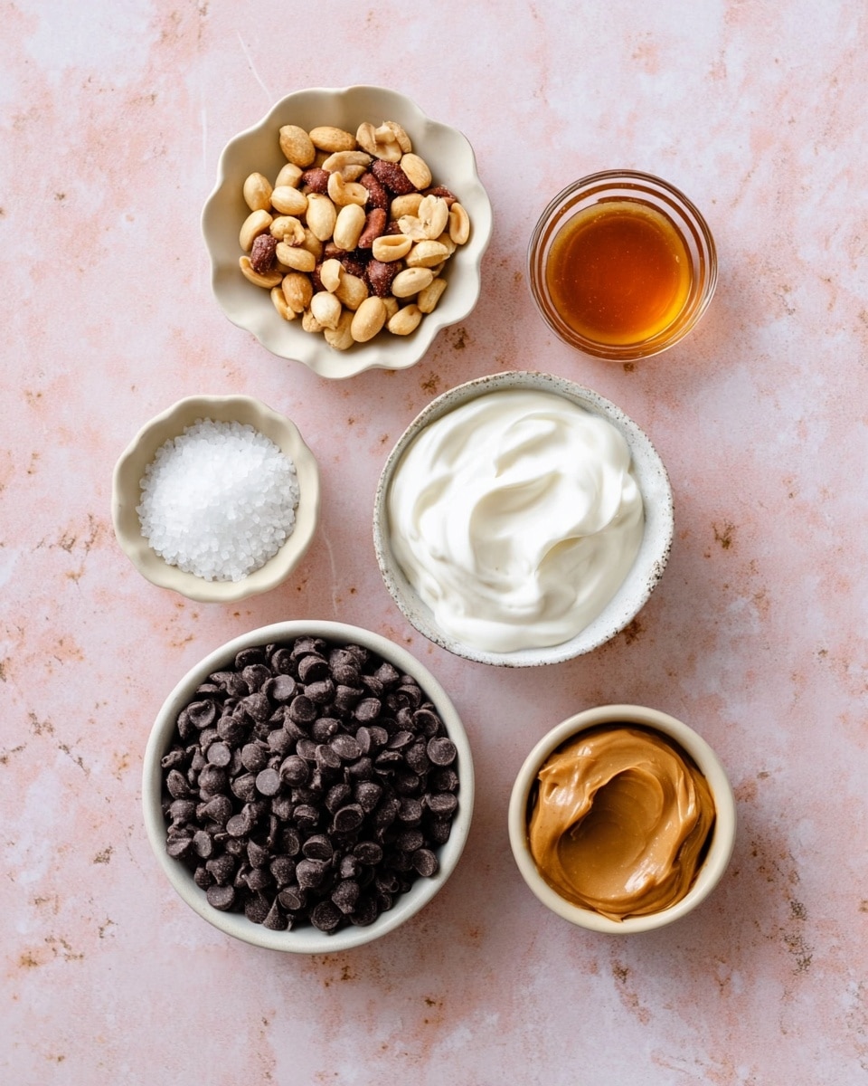 Seven small bowls of ingredients sit on a white marbled surface with a light pink tint. The largest bowl at the bottom right is filled with many dark chocolate chips, small and round, showing a matte texture. Above it, a white bowl holds smooth, thick white yogurt with gentle swirls on top. To the left of the yogurt, a scalloped bowl contains golden-brown dry roasted peanuts with some reddish skin still on. Above the peanuts are two small light beige bowls; the top one has a soft white coconut oil scoop, and the other below it has white flaky sea salt. At the top right is a small glass bowl filled with amber-colored liquid, smooth and glossy. The last bowl, at the bottom left, contains tan creamy peanut butter with a shiny surface. All bowls are neat and evenly spaced in a casual, inviting arrangement. Photo taken with an iphone --ar 4:5 --v 7