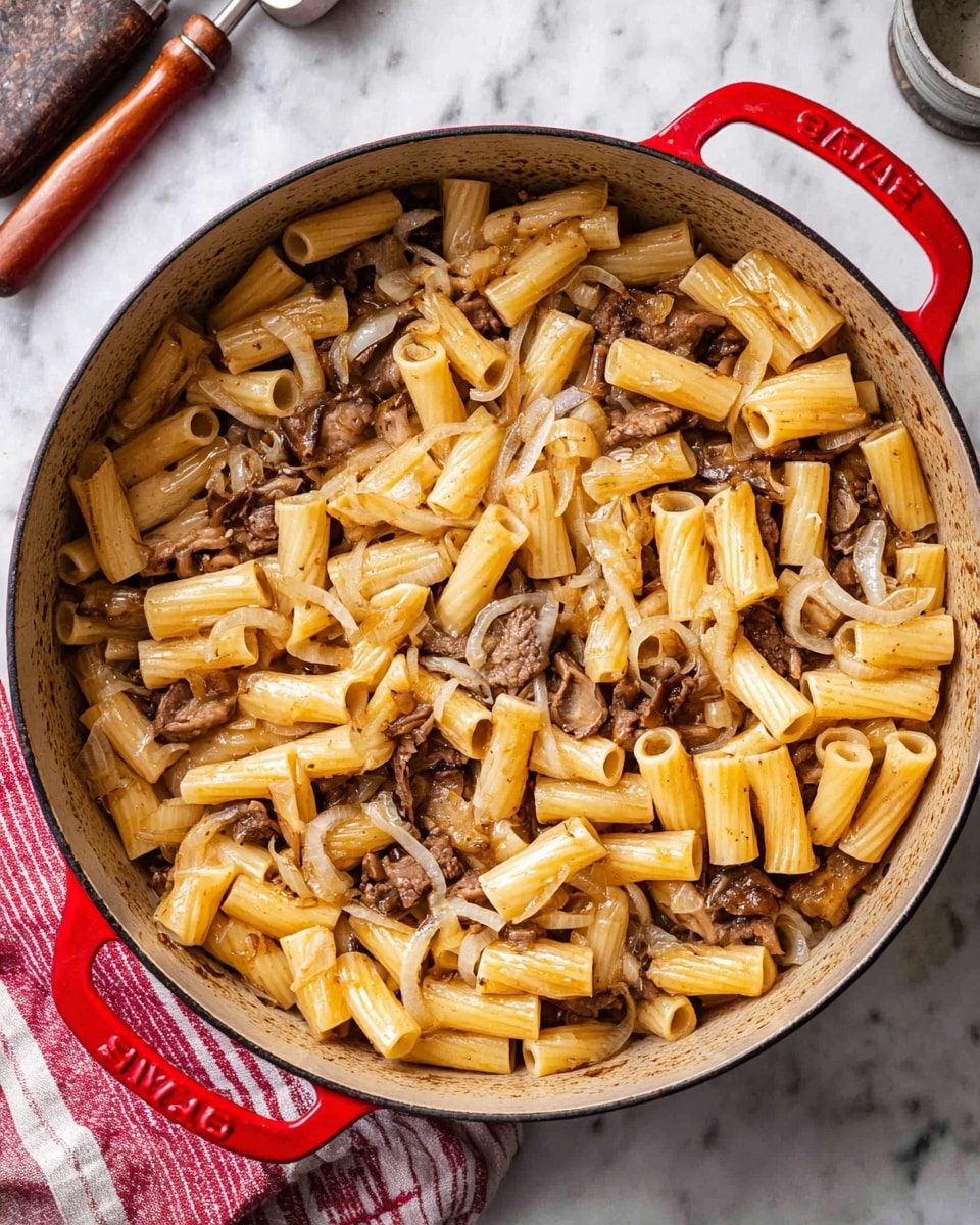 This image shows a red pot filled with pasta dish. The bottom layer is a mix of tubular pasta in a light golden color and tender brown pieces of beef or mushrooms, all coated with a light sauce that gives a slight shine. The pasta shapes are evenly spread, with some pieces laying flat and others standing upright. Thin slices of cooked onions add texture and a slightly translucent pale layer throughout. The pot is placed on a white marbled surface with some kitchen tools and a red and white striped cloth nearby. Photo taken with an iphone --ar 4:5 --v 7