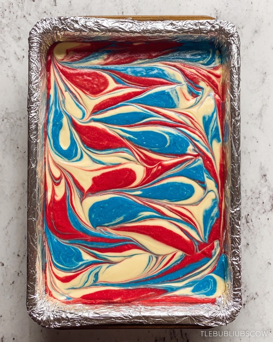 The image shows a rectangular baking pan lined with foil, filled with a colorful swirl pattern of batter. The batter has three main colors: bright red, blue, and creamy white. These colors mix in a marbled way, creating curved, twisted patterns across the whole top layer. The foil around the edges is slightly crinkled, and the pan rests on a white marbled surface. Photo taken with an iphone --ar 4:5 --v 7