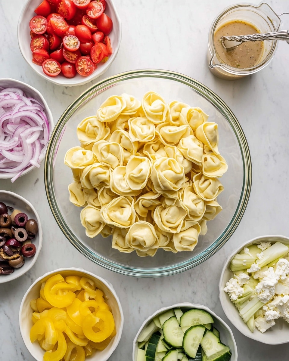 A large clear glass bowl filled with three layers of pale yellow tortellini pasta sits in the center on a white marbled surface. Surrounding the bowl, there are seven small white bowls with fresh and colorful ingredients: halved red cherry tomatoes at the top left, thinly sliced purple onions below them, a light brown bowl with thin bright yellow pepper slices to the right, a few dark brown olive slices in a white bowl nearby, chopped pale artichokes in a white bowl near the bottom right, thin cucumber slices in a white bowl at the bottom left, and crumbled white cheese in a small white bowl next to the cucumbers. A clear glass container filled with light brown dressing and a metal stirrer is placed at the top right. The composition is bright and clean. Photo taken with an iphone --ar 4:5 --v 7