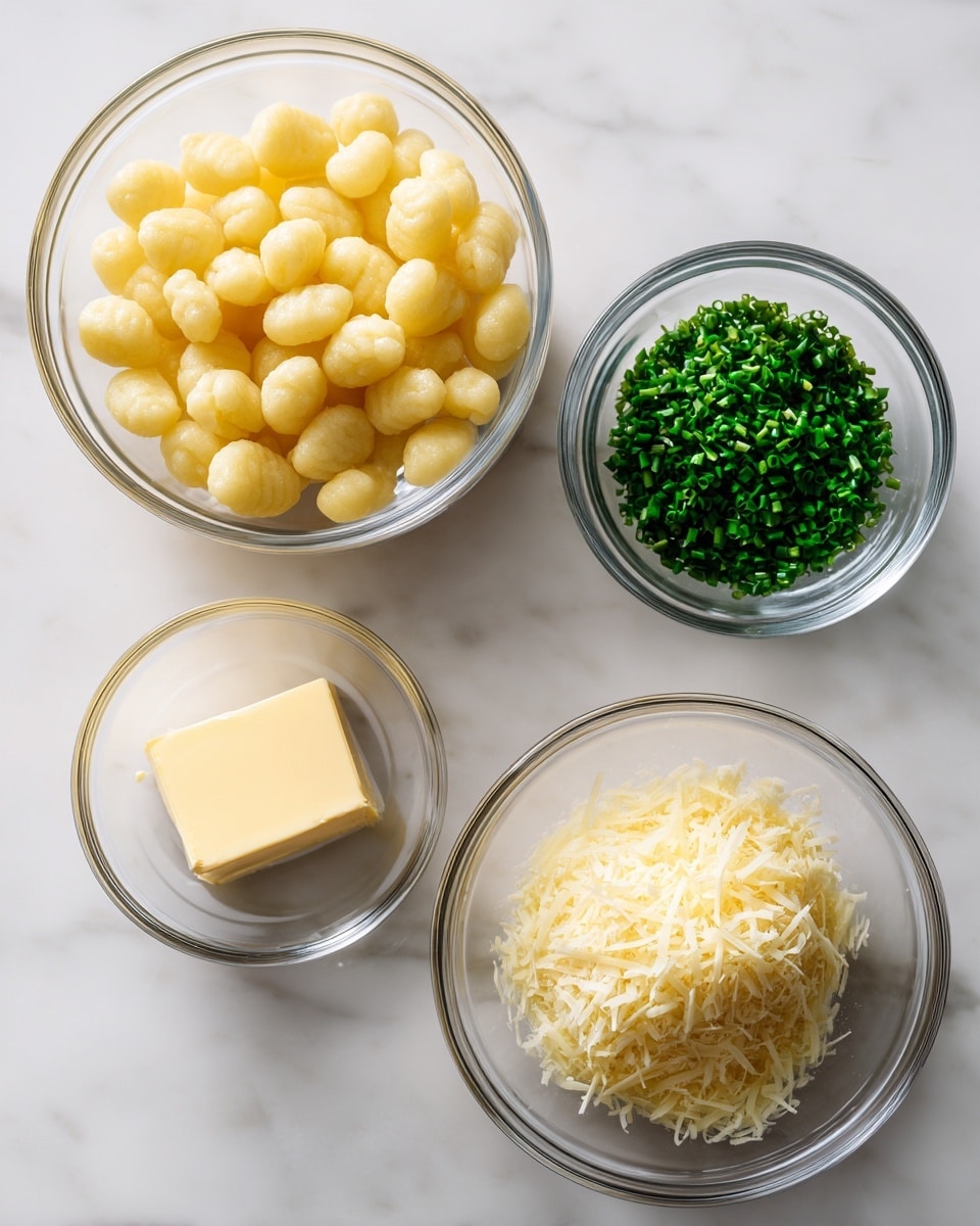 The image shows four clear glass bowls arranged on a white marbled surface. The largest bowl on the left is filled with light yellow round gnocchi pieces. To the top right is a small bowl with finely chopped dark green chives. Below it, a medium-sized bowl contains a mound of pale yellow grated parmesan cheese with a slightly grainy texture. At the bottom left is a small bowl holding a single square piece of pale yellow unsalted butter with a smooth texture. Each ingredient is clearly visible and neatly presented. photo taken with an iphone --ar 4:5 --v 7