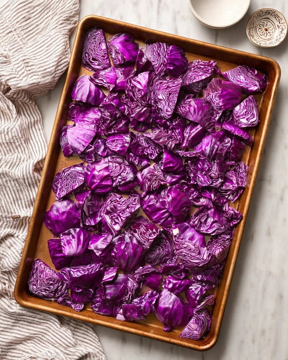 A baking tray filled with many pieces of bright purple-red cabbage, unevenly shaped and spread evenly across the tray. Each cabbage piece shows a mix of smooth and slightly wrinkled textures, with swirls of lighter purple and white lines visible on some pieces. The tray is a rich bronze color, and it sits on a white marbled surface. Near the top edge of the image, there is a small white ceramic bowl and a decorative dish partially visible, along with a soft striped cloth on the left side. Photo taken with an iphone --ar 4:5 --v 7