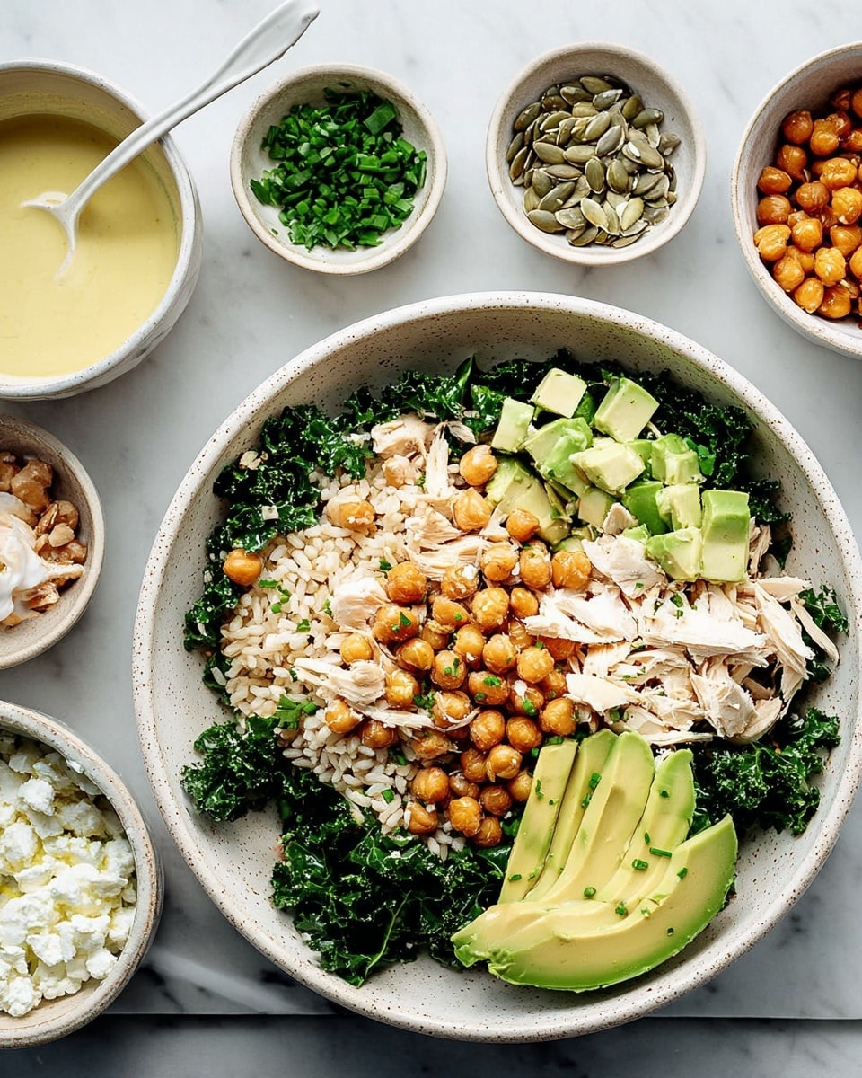 A white speckled bowl holds a layered dish on a white marbled surface. The bottom layer is light brown rice filling most of the bowl, topped with dark green kale leaves scattered around. On top of the kale and rice are chunky pieces of shredded white chicken meat and small cubes of light green avocado. Roasted golden chickpeas are sprinkled over all the layers, adding texture and color. Around the main bowl, smaller white bowls hold sunflower seeds, crispy chickpeas, white cottage cheese, chopped fresh green chives, and a bowl with creamy yellow dressing and a white spoon. Photo taken with an iphone --ar 4:5 --v 7